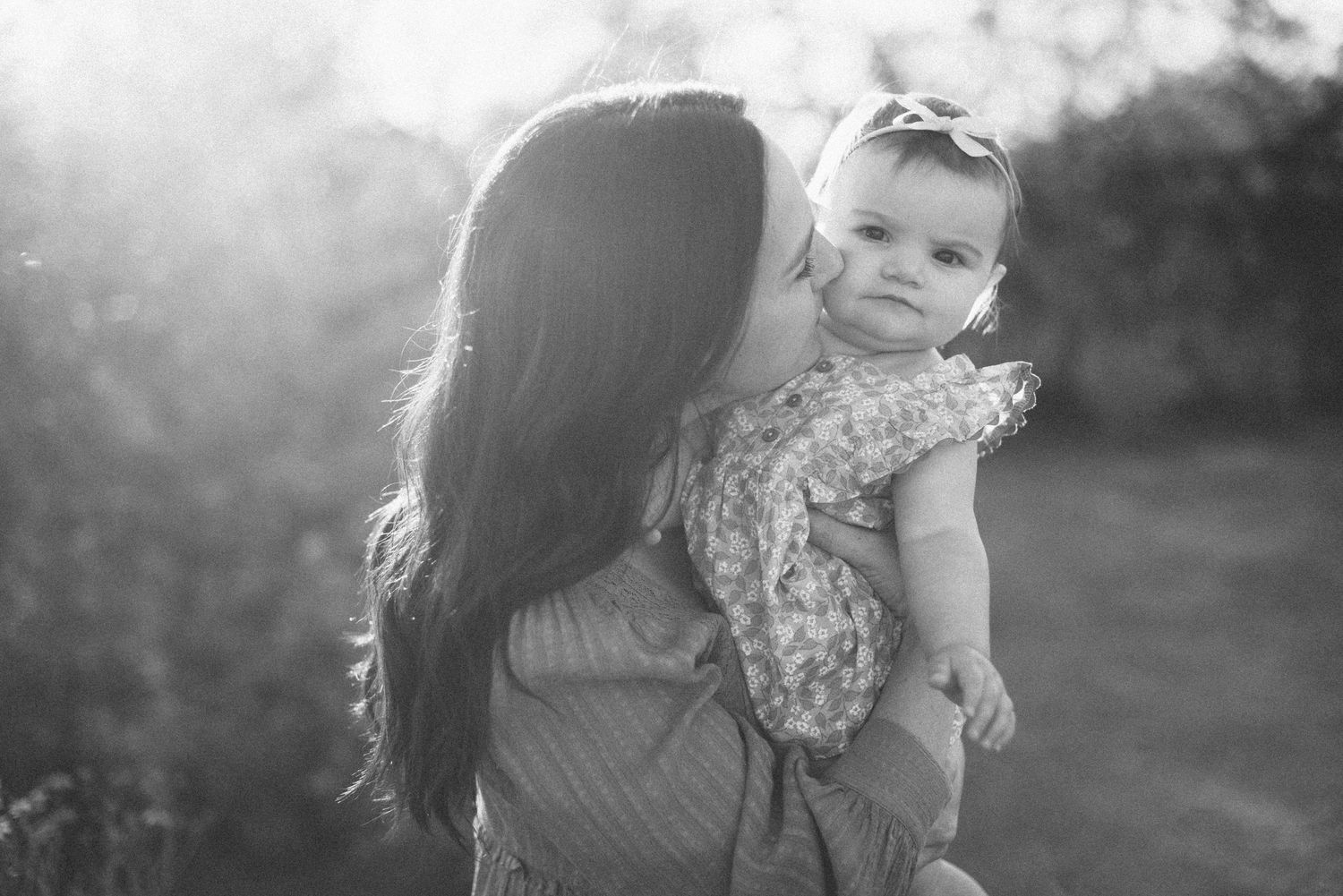 Black and white portrait of mother and baby outdoors at sunset.