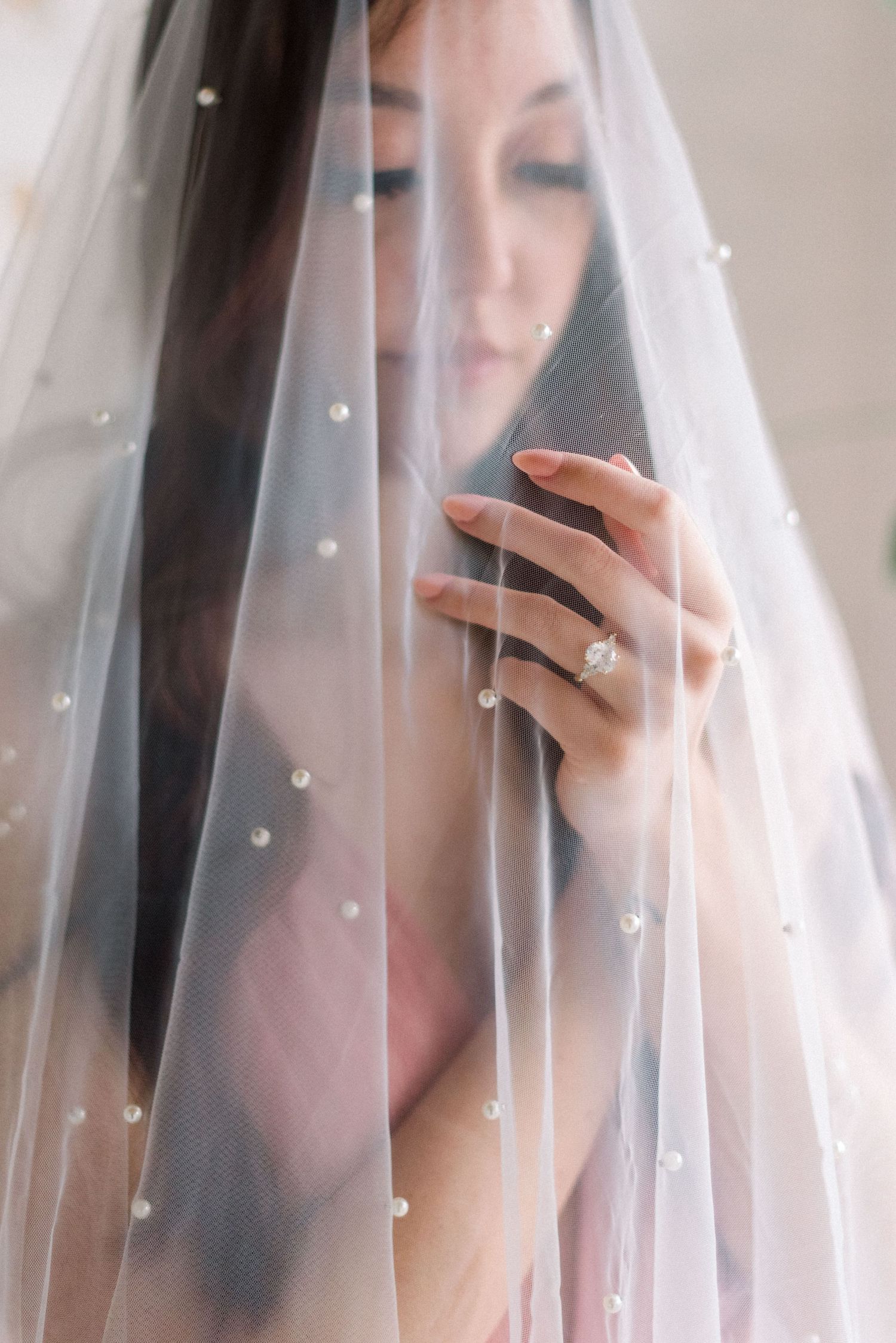 Close-up of hand with engagement ring through delicate dotted veil.