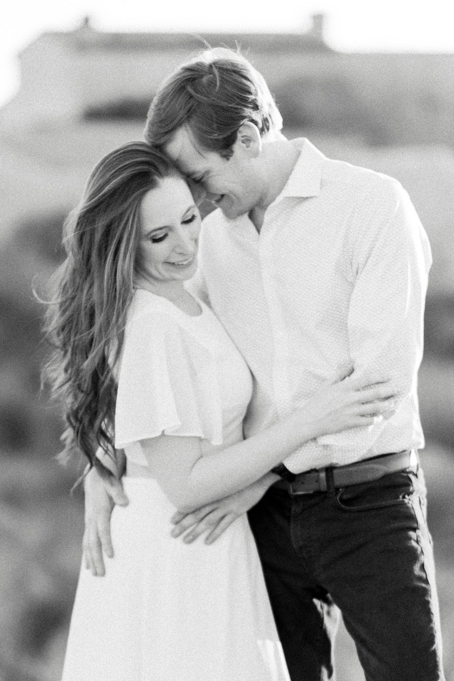 A romantic black and white portrait of an engaged couple embracing in soft natural light.