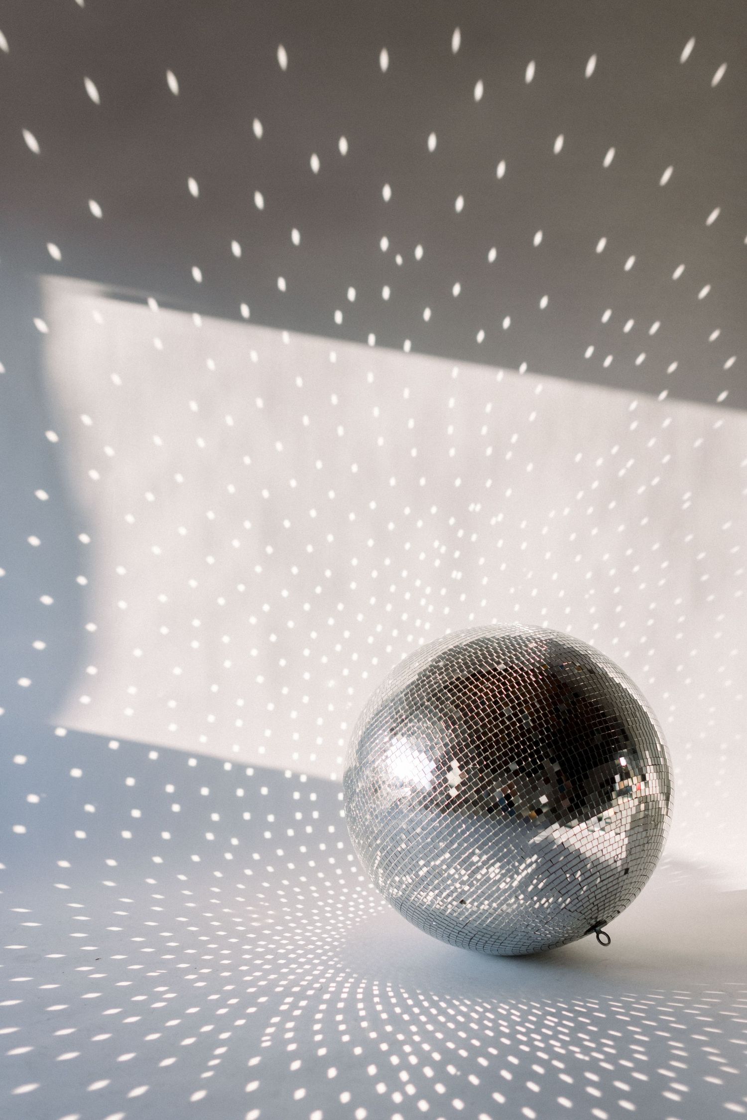 Silver disco ball creating sparkly light pattern effect on white wall.