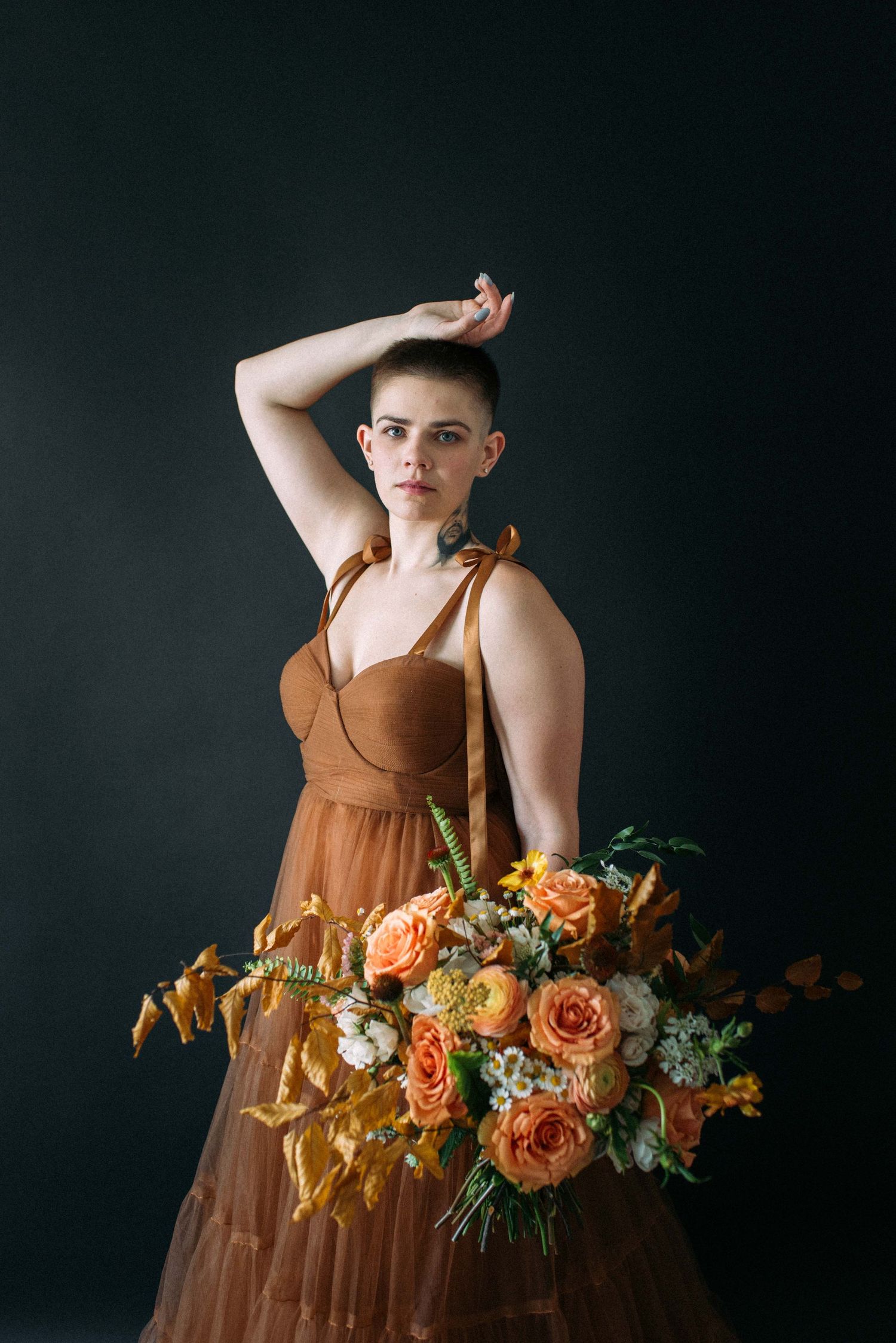 A studio portrait featuring a brown dress and vibrant orange and peach floral bouquet.
