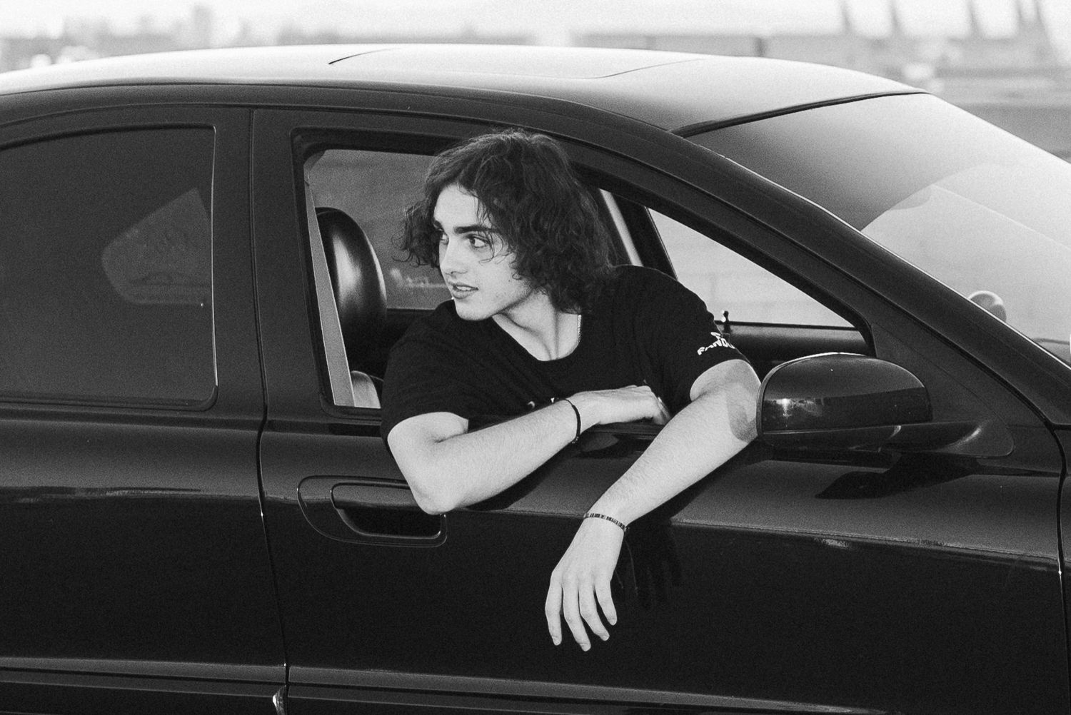 Person leaning out of black car window in monochrome photo.