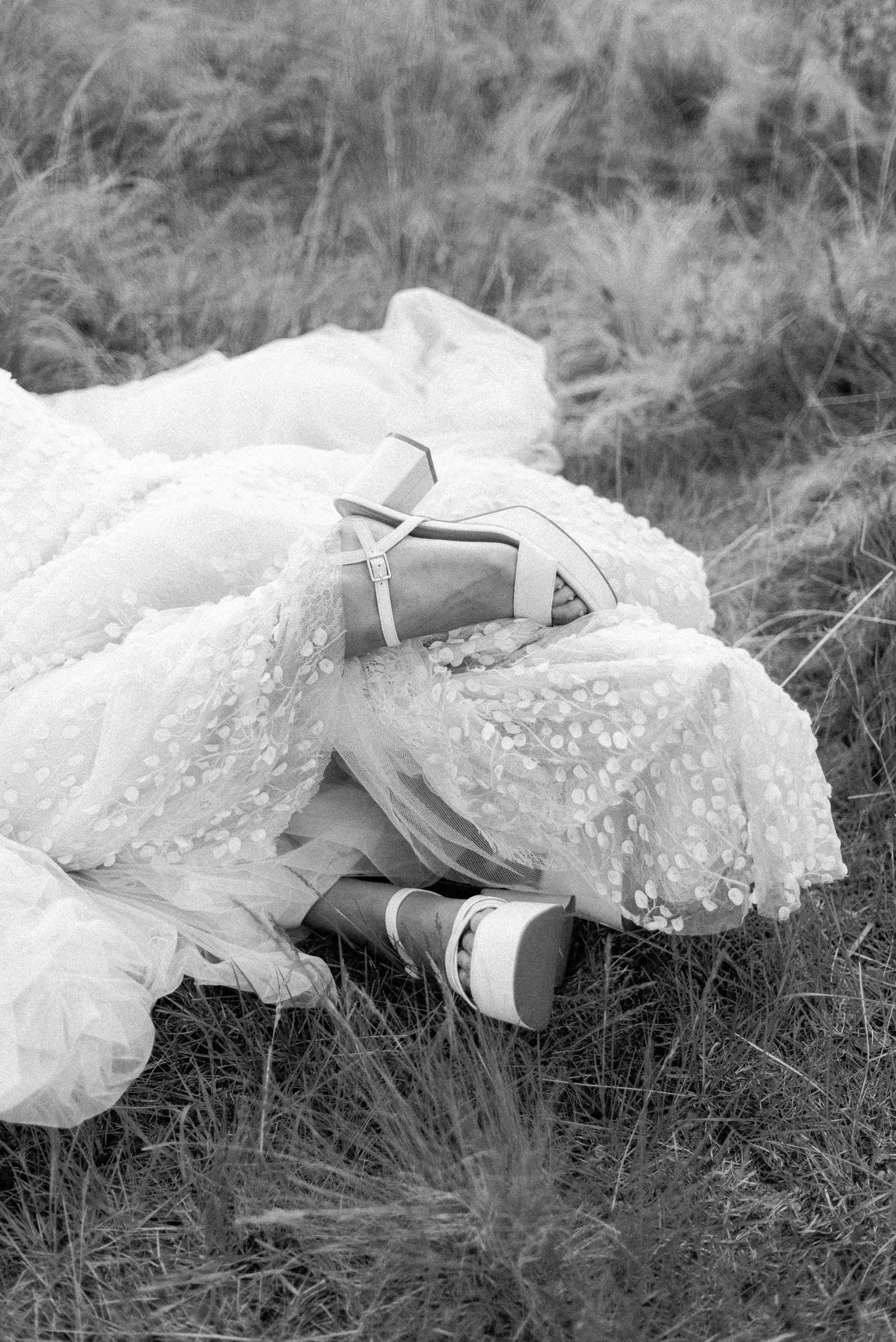 Wedding shoes and lace dress details laying in tall grass.