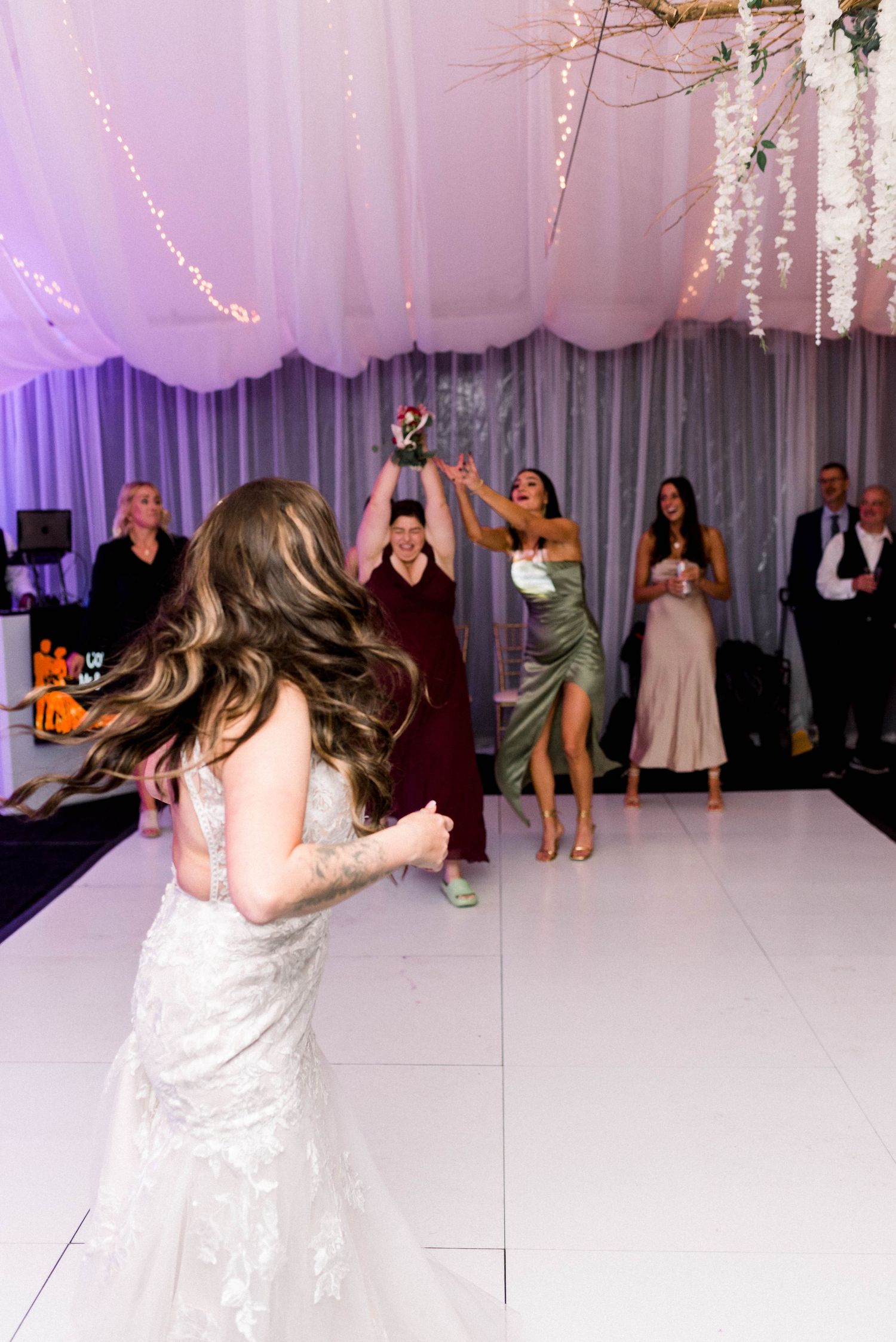 Wedding guests catching the bouquet at reception with bride in foreground.