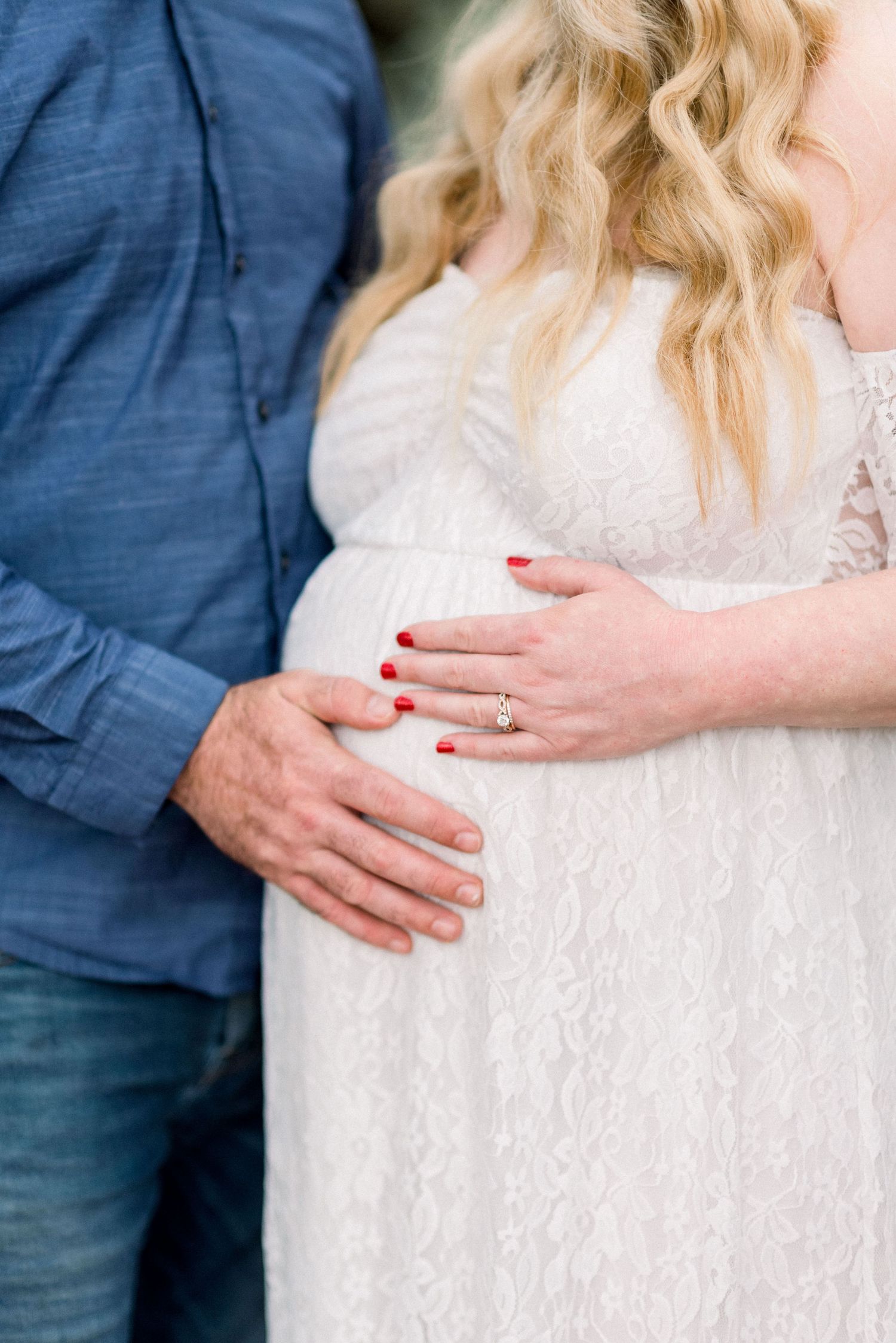 Close-up of hands cradling a pregnant belly in white lace maternity dress.