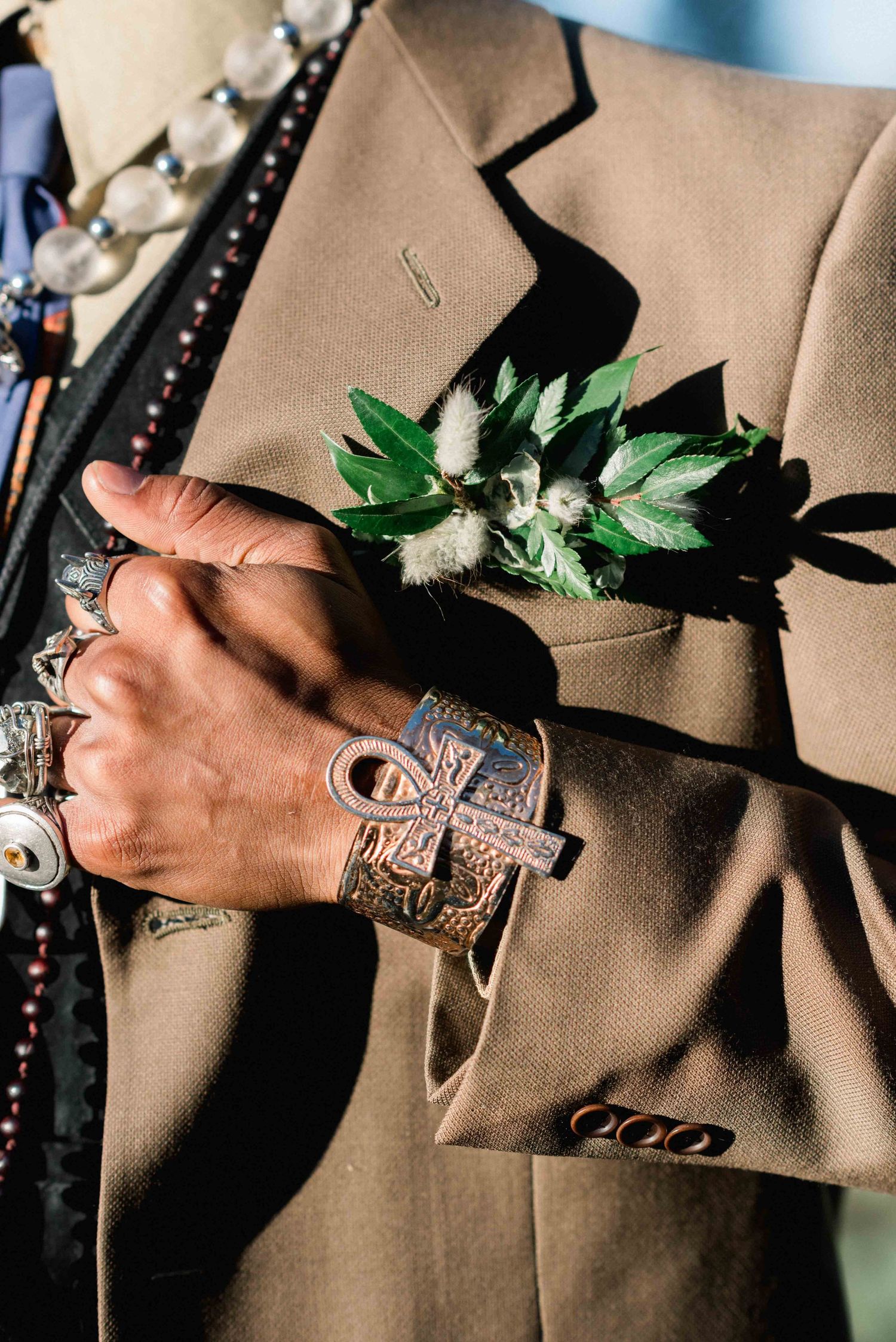 Detail shot of ornate jewelry and boutonniere on tan suit jacket.