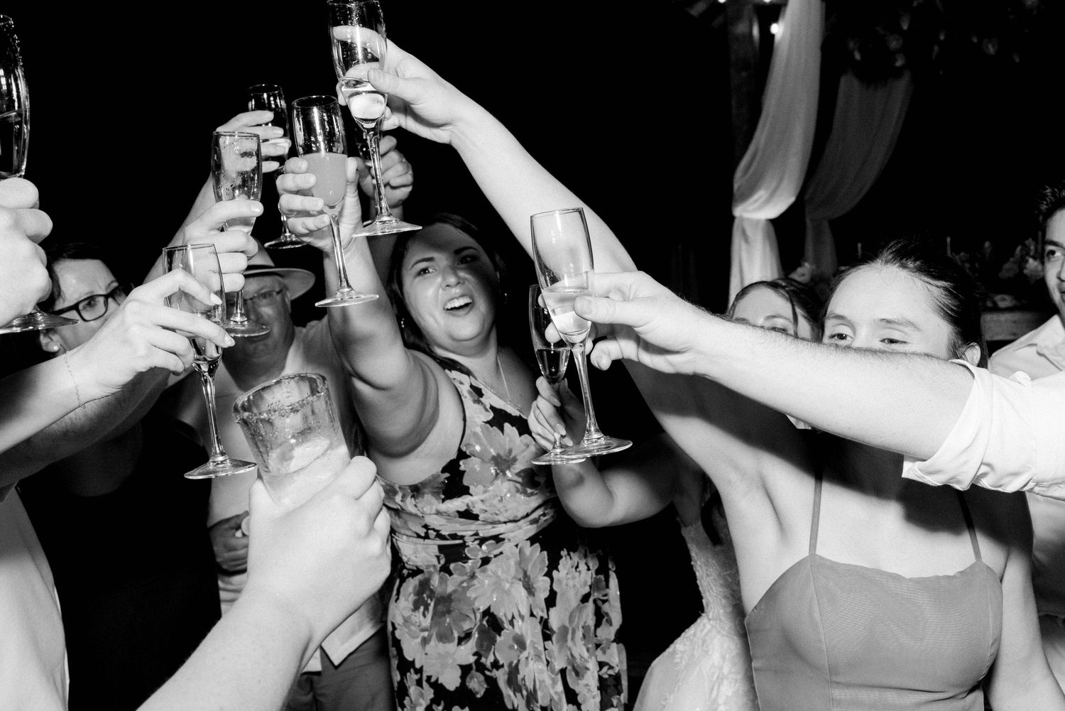Wedding guests raise champagne glasses in a joyful toast during an outdoor celebration.