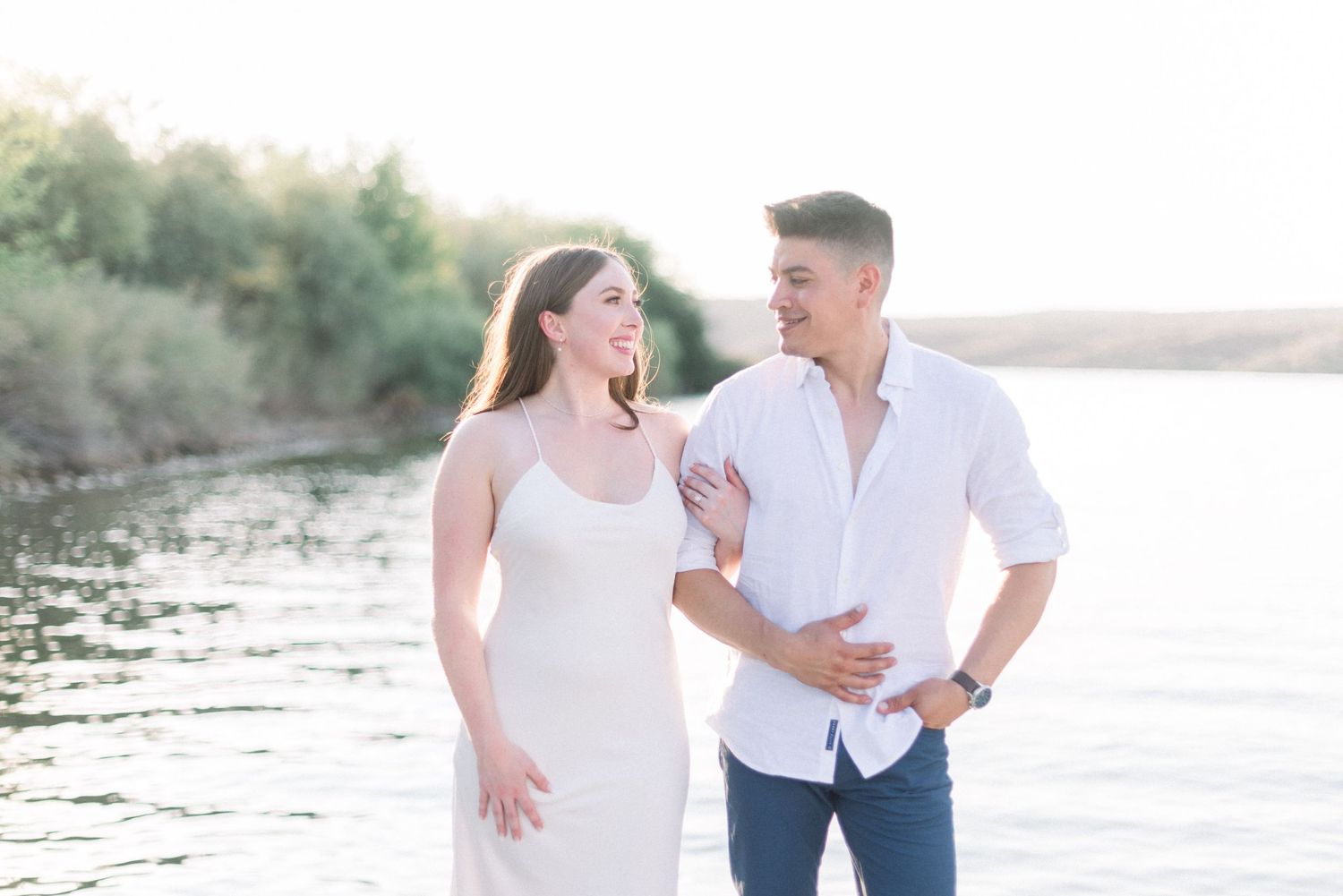 A couple sharing a joyful moment together on a lakeside beach at sunset.