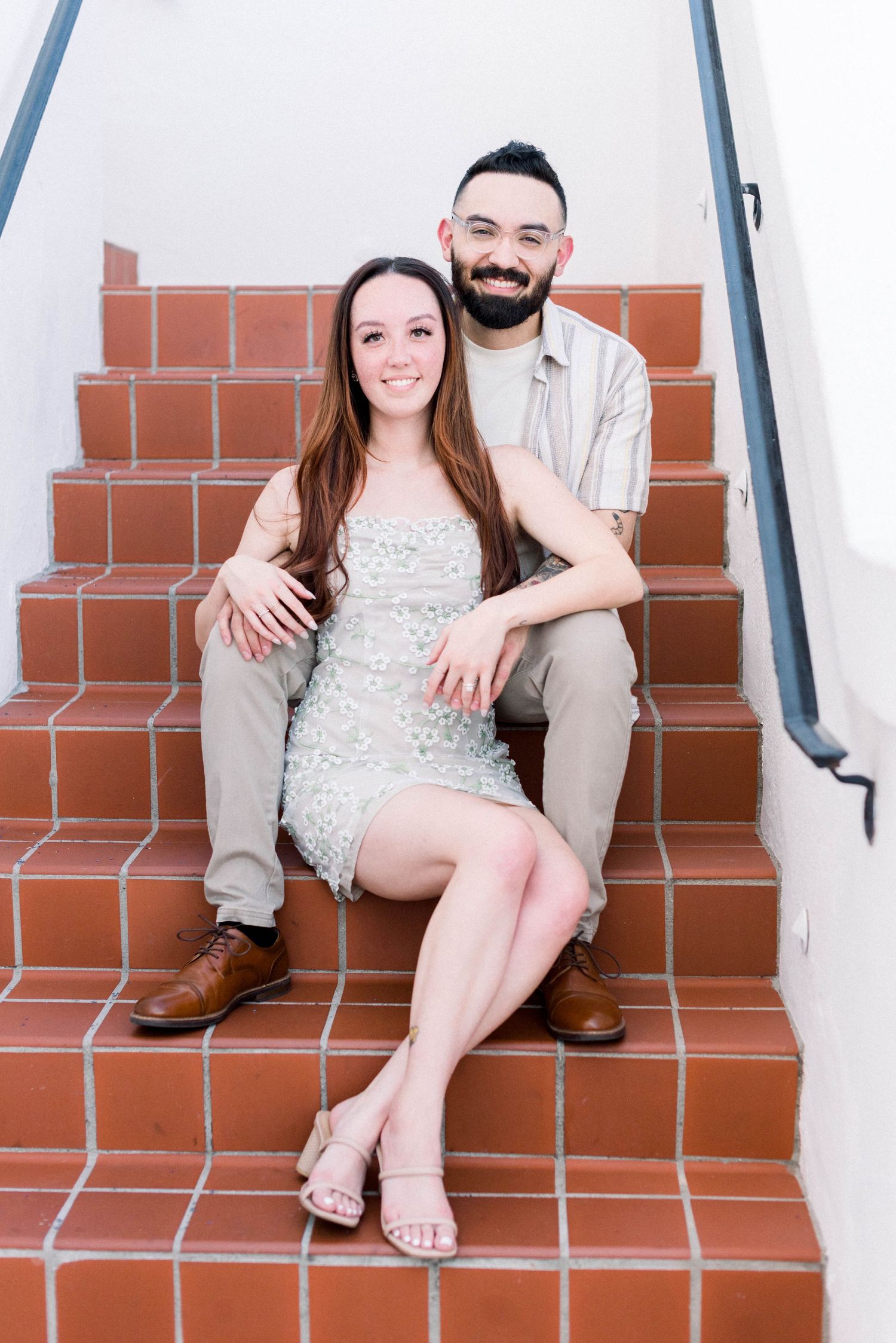 A couple sits together on terracotta steps during an engagement photoshoot.