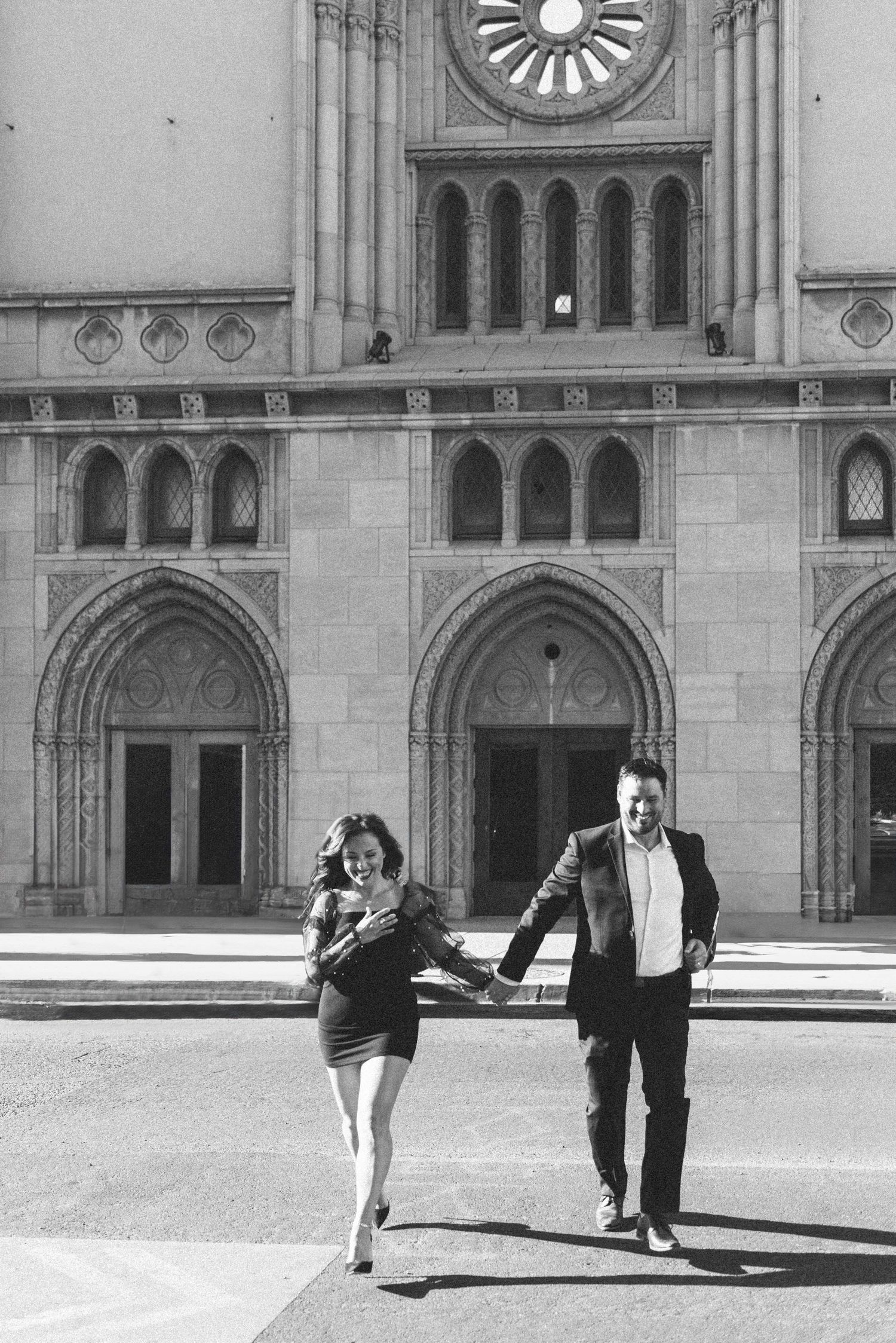 Black and white photo of couple running in front of historic building facade.