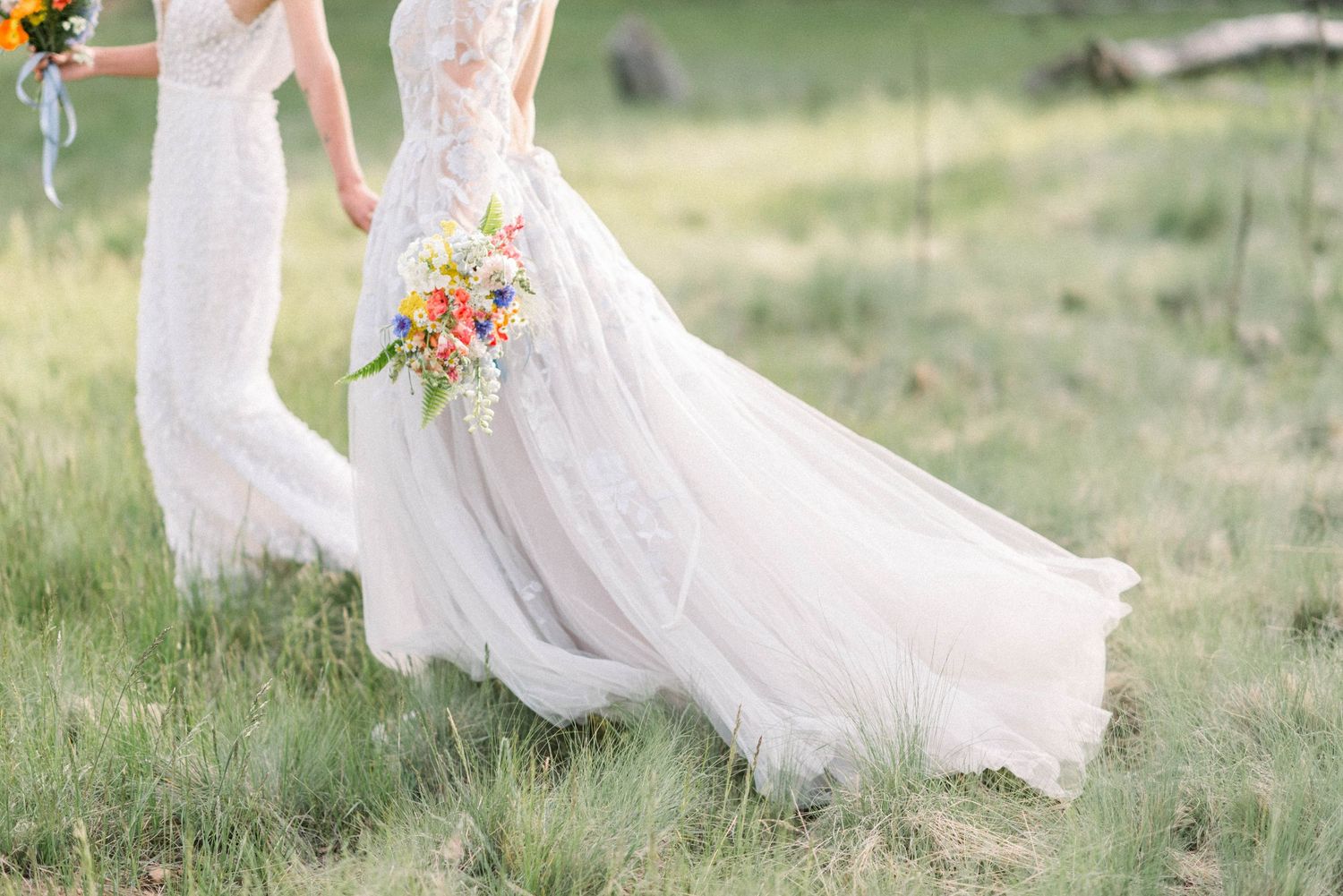 Elegant white wedding dress flowing in the breeze with vibrant orange and yellow wildflower bouquet in a grassy meadow.