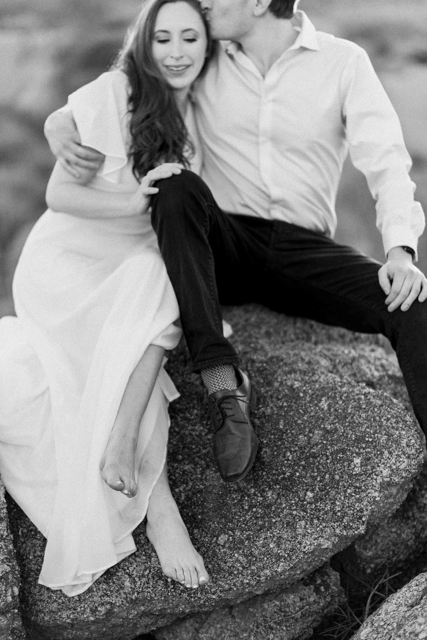 Intimate black and white portrait of a couple sitting together on a rocky outcrop.