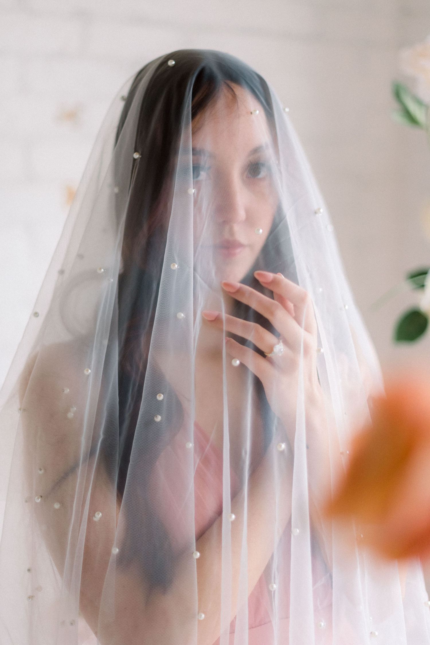 A dreamy bridal portrait through a sheer veil with delicate pearl details against a light background.