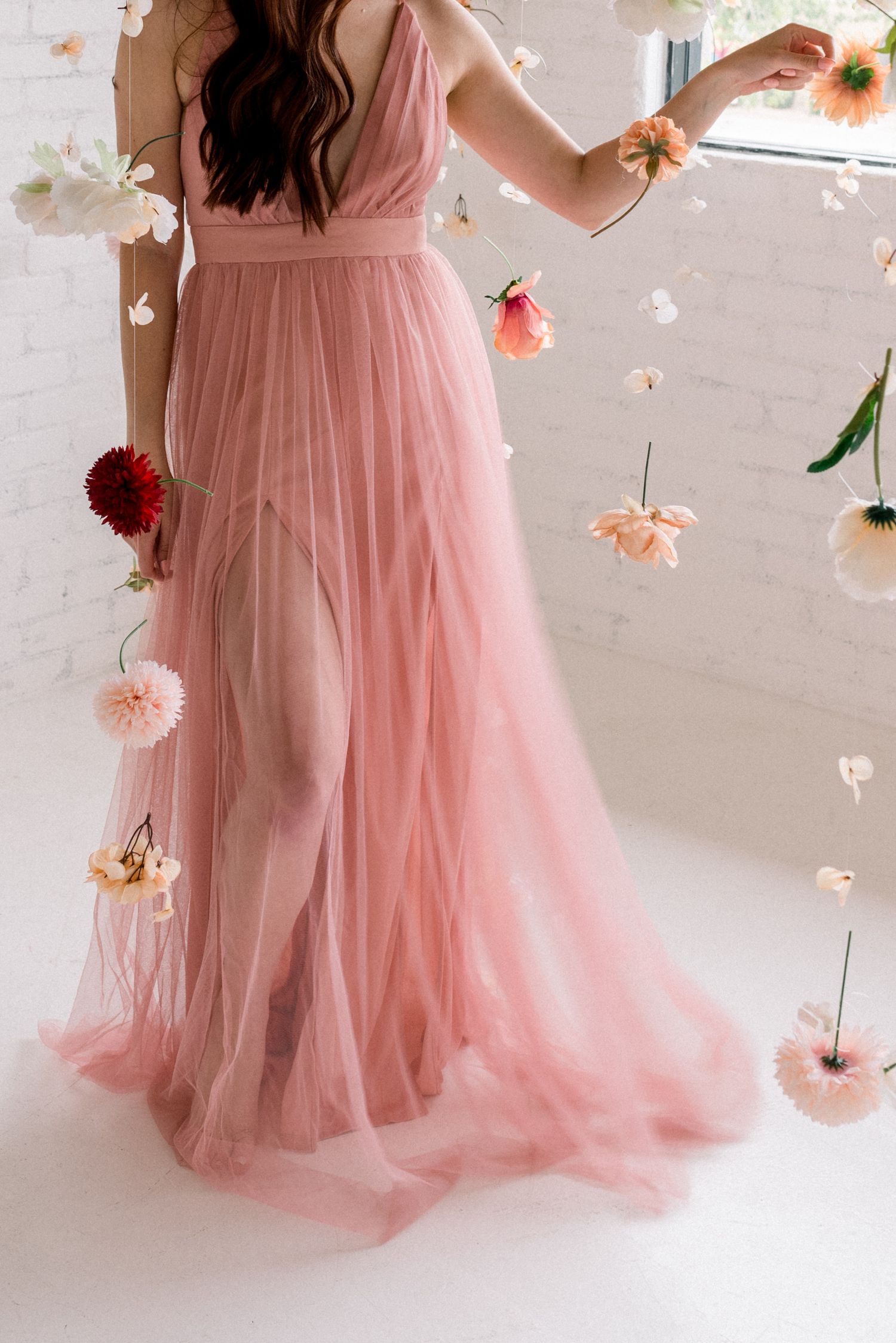 Flowing pink tulle gown with romantic floating flower petals in a dreamy indoor setting.