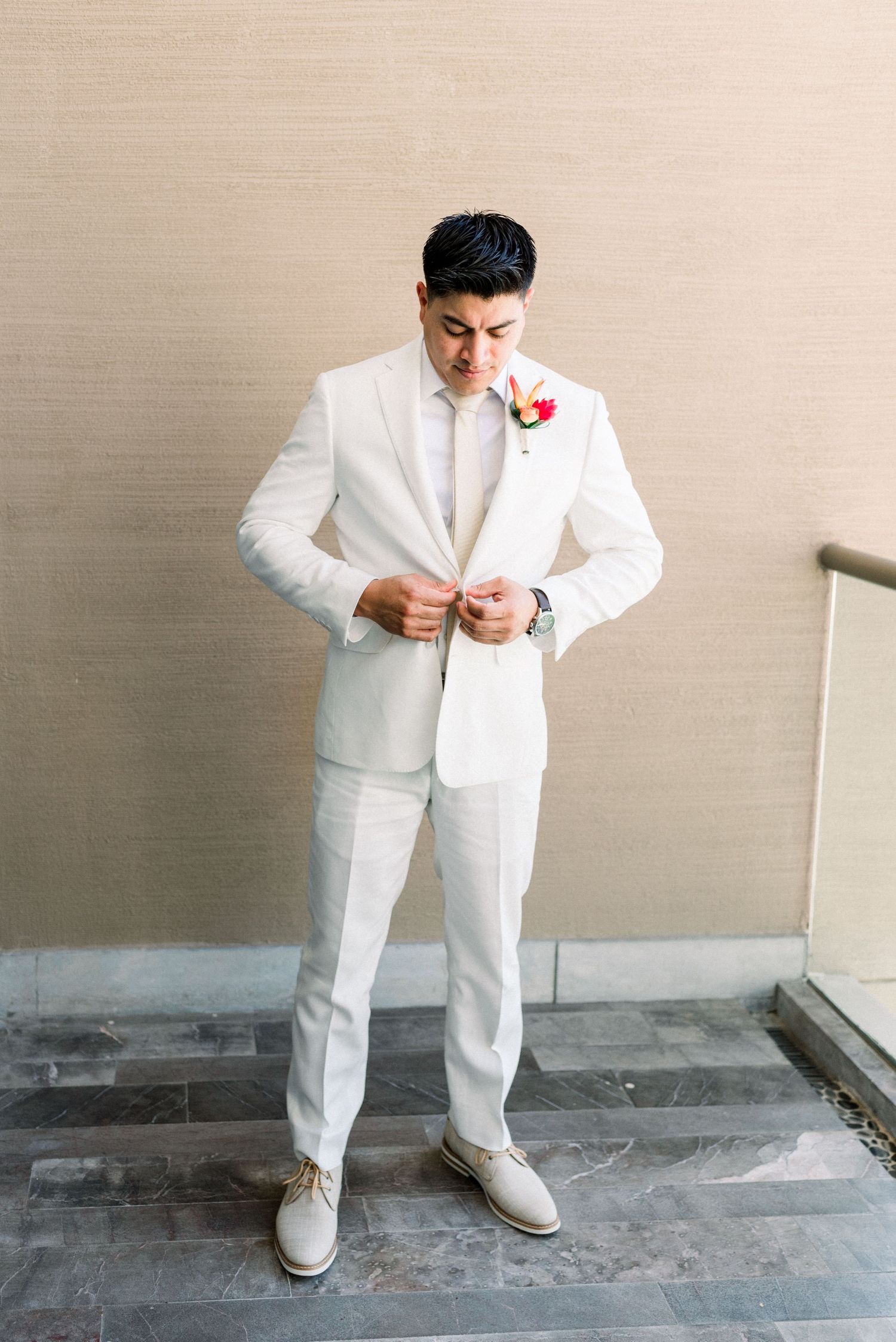 Groom in all-white suit and matching shoes adjusting his jacket buttons.