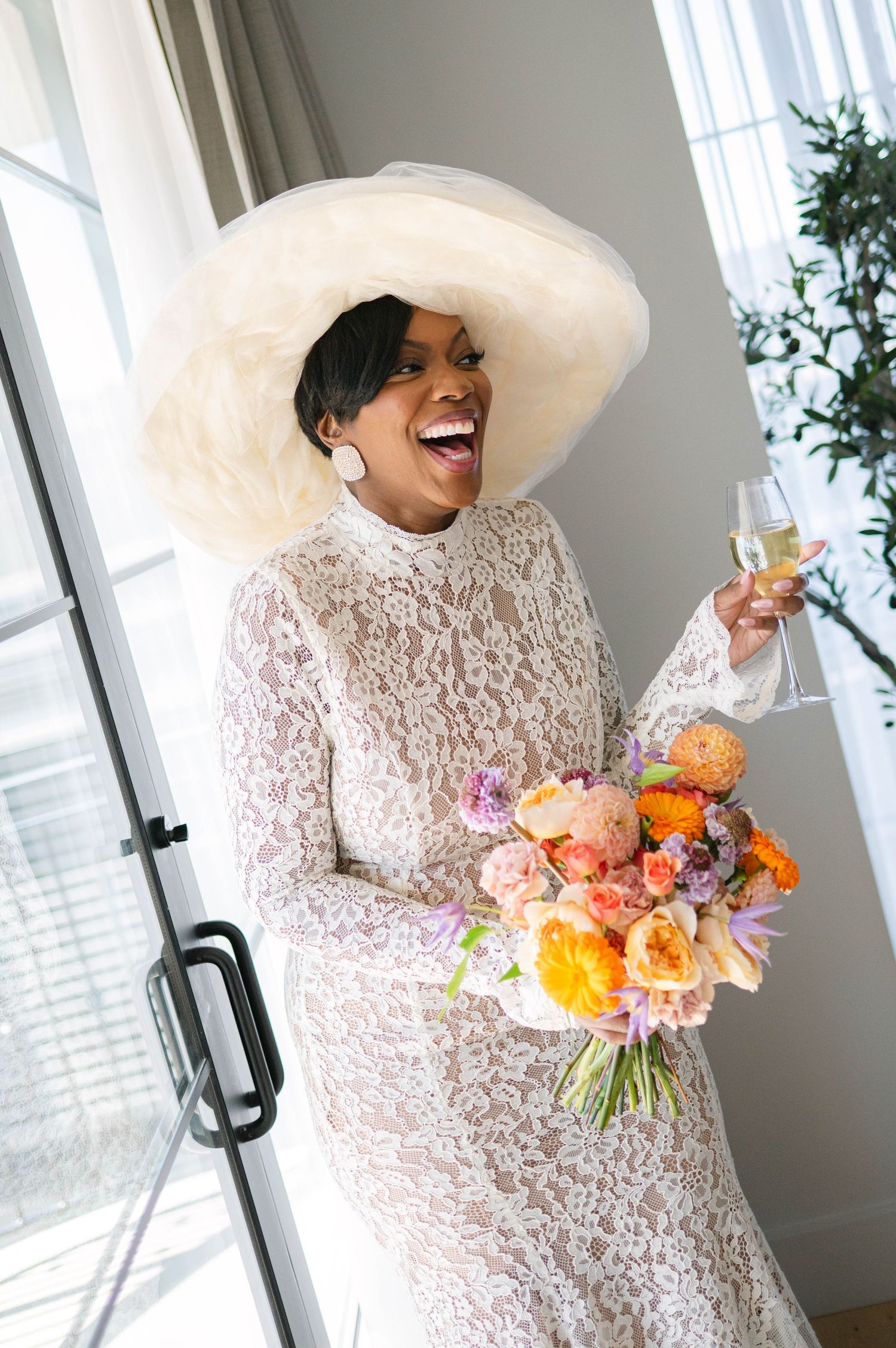A joyful moment captured in a bright room with someone wearing a wide-brimmed hat and holding vibrant flowers.