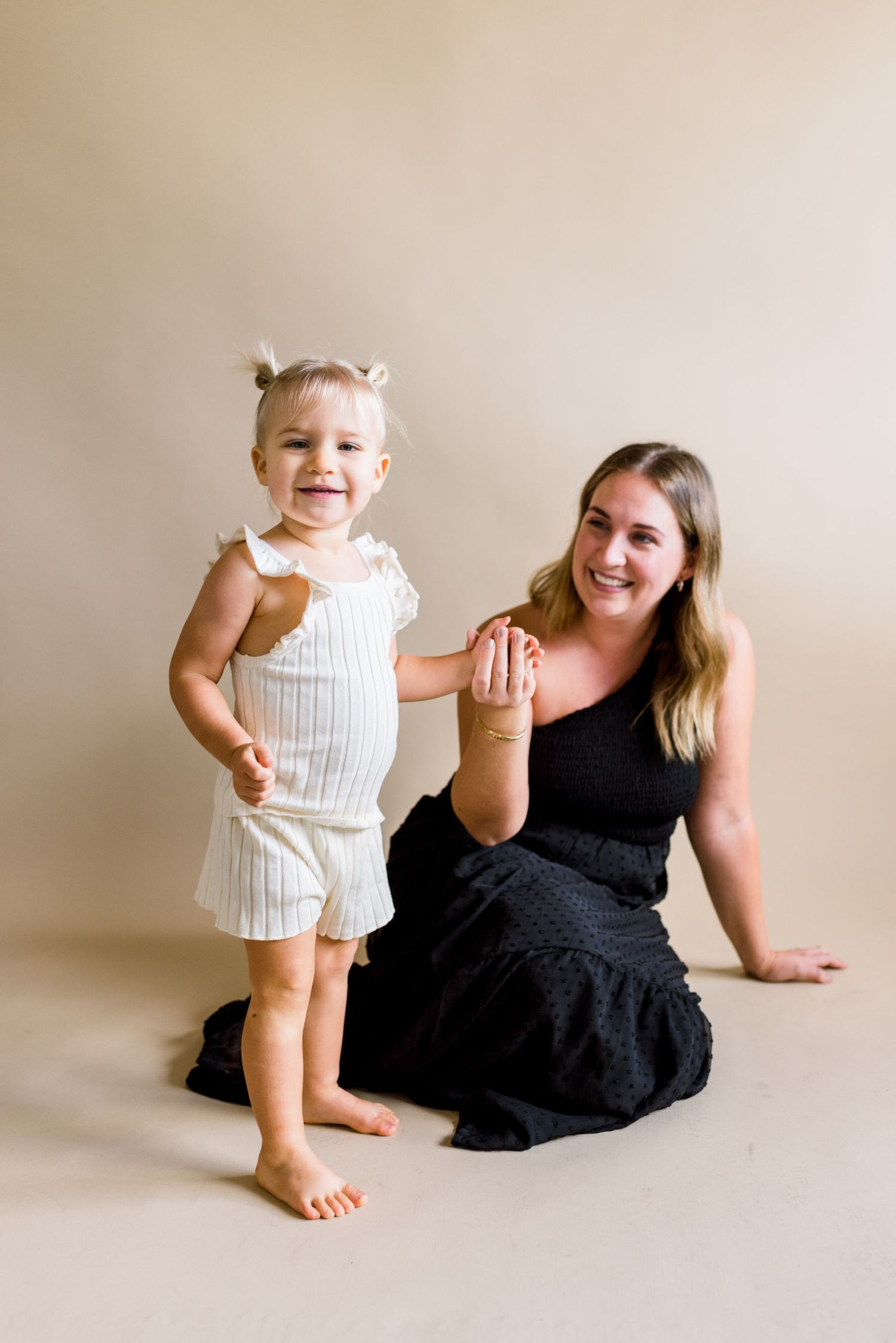 A studio portrait showing playful interaction between two people against a beige background.