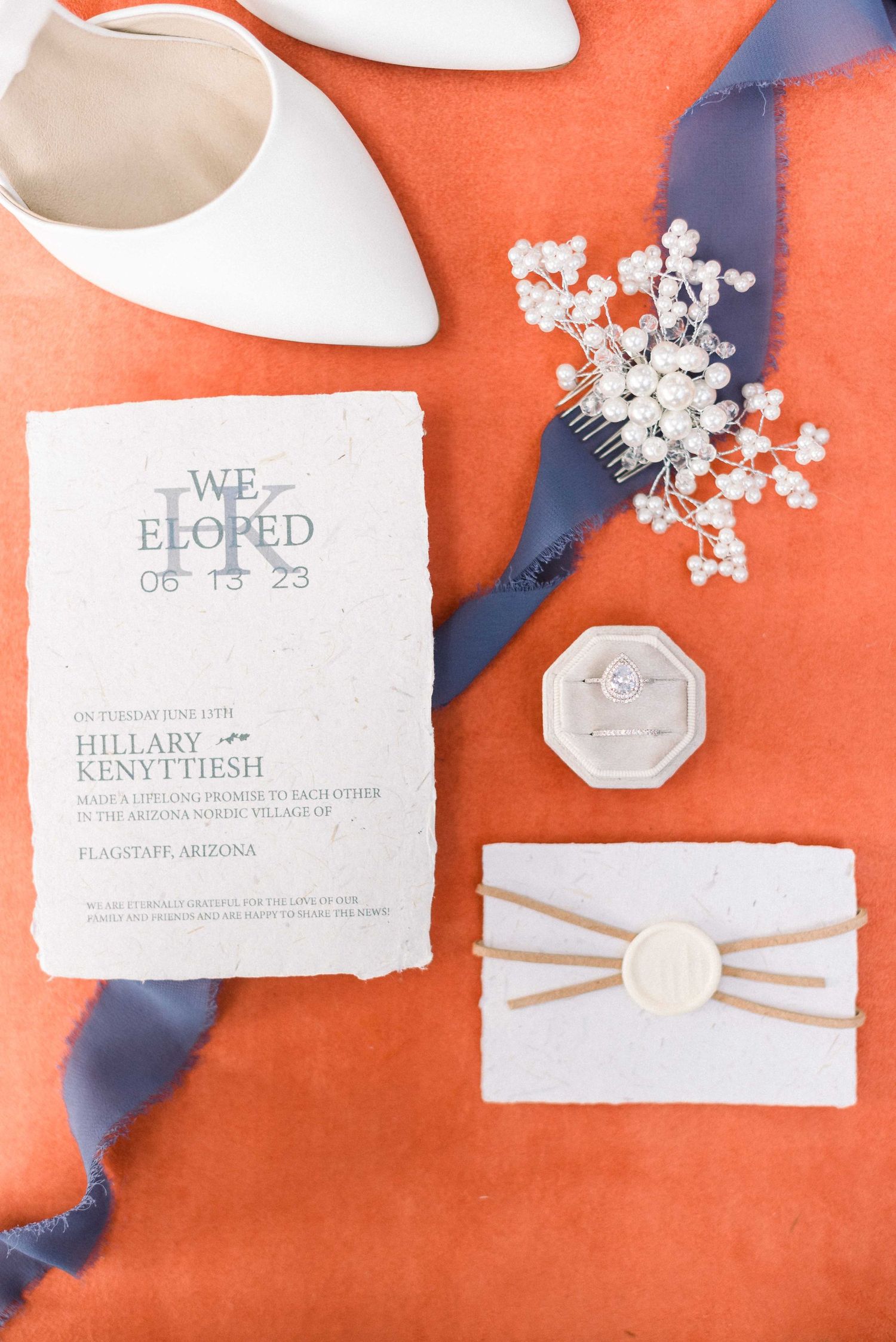 Elopement announcement with white pointed shoes and delicate floral accessories on coral background.