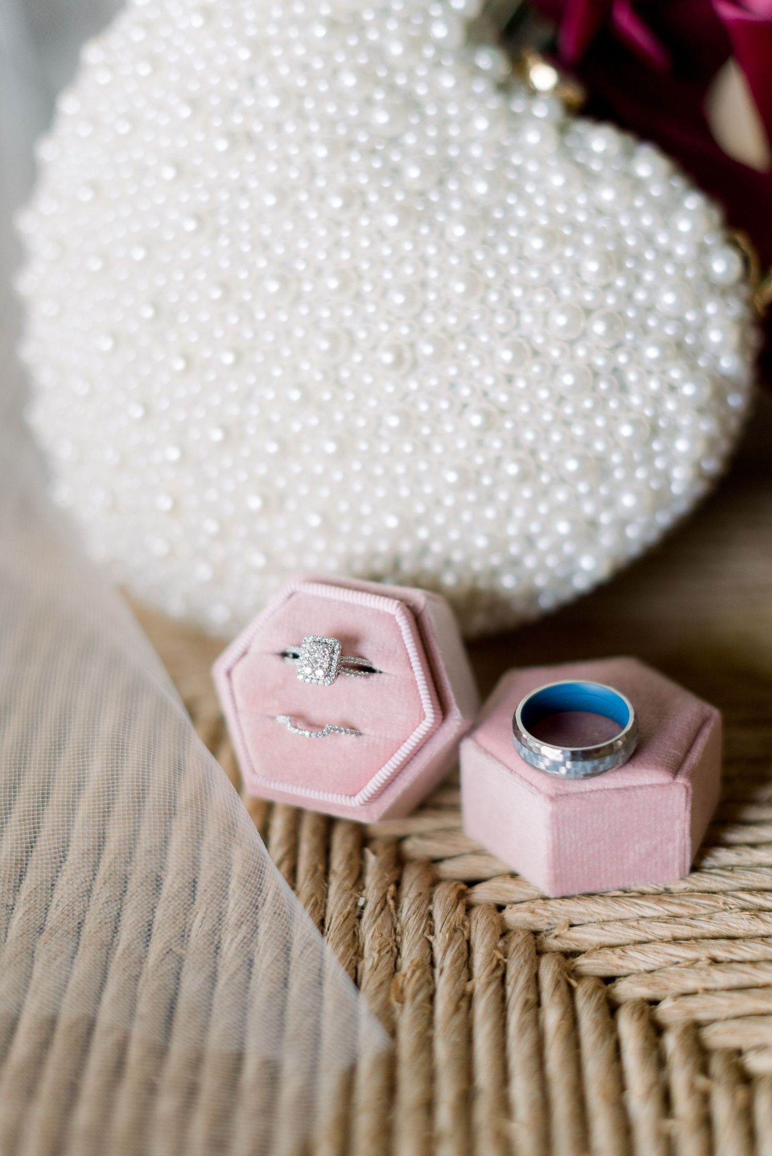 Wedding rings displayed in pink hexagonal boxes beside pearl-studded accessory.