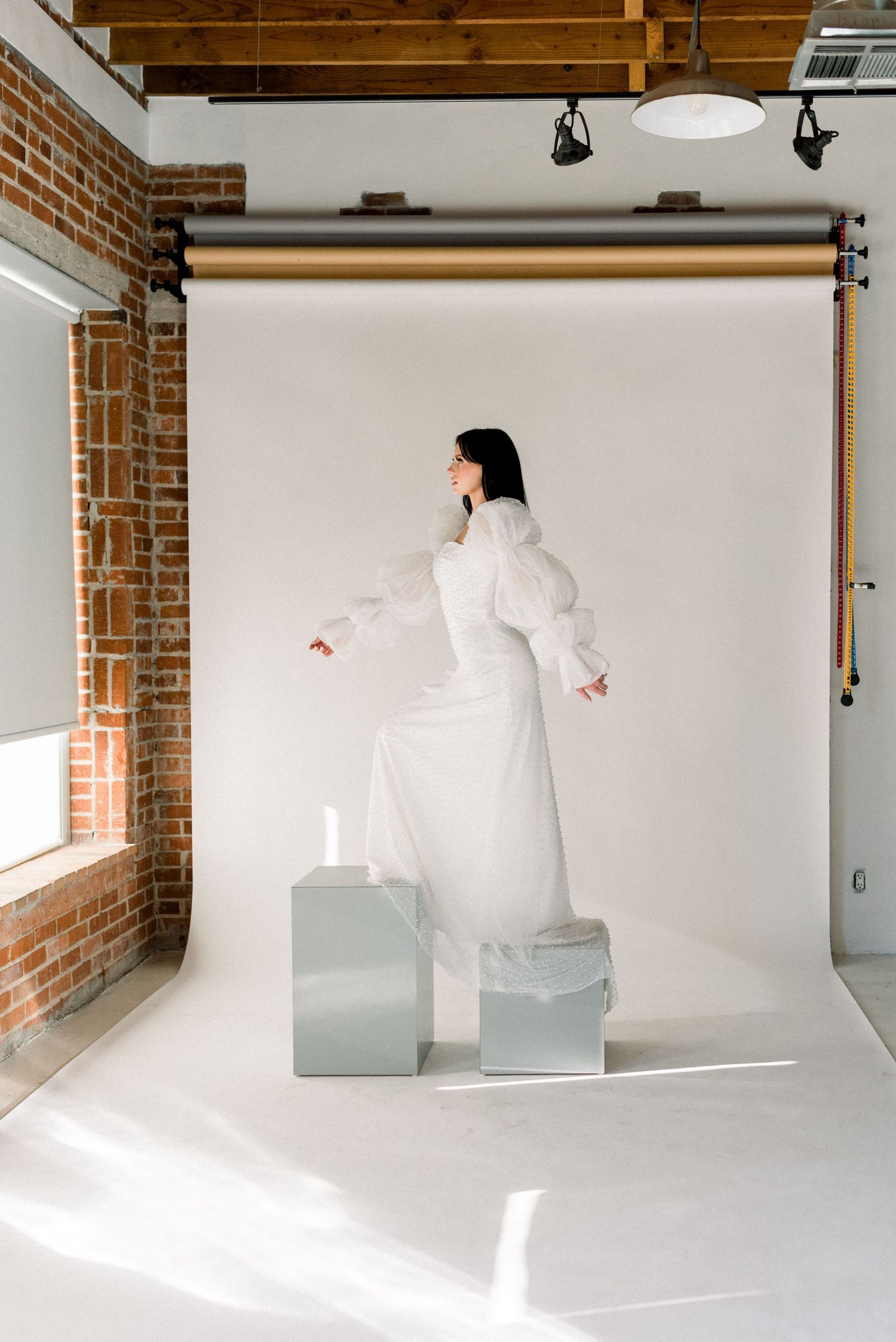 Fashion editorial shot of model in white dress standing on geometric blocks in studio setting.