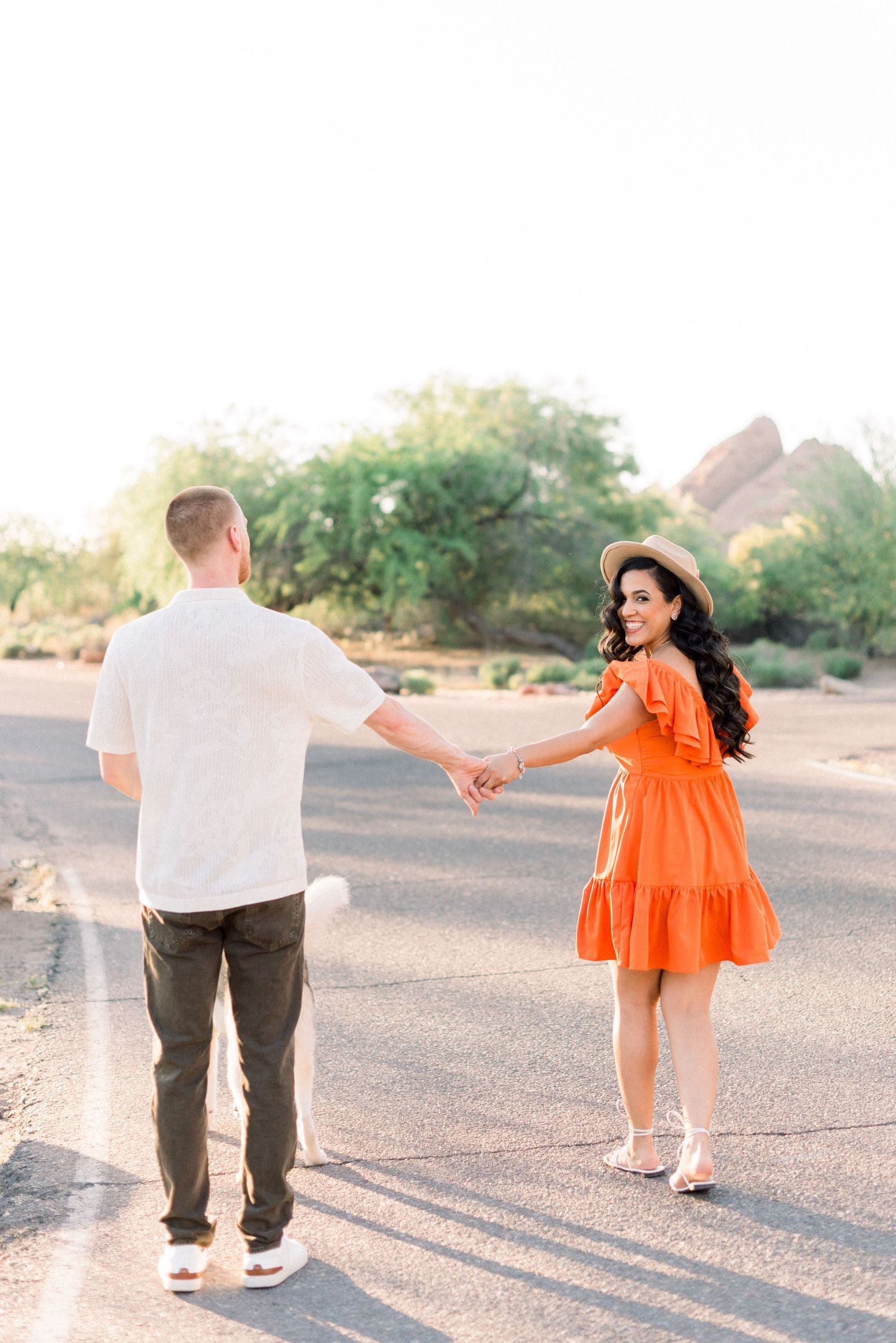 Couple holding hands while walking in desert setting, her in orange dress and him in white shirt.