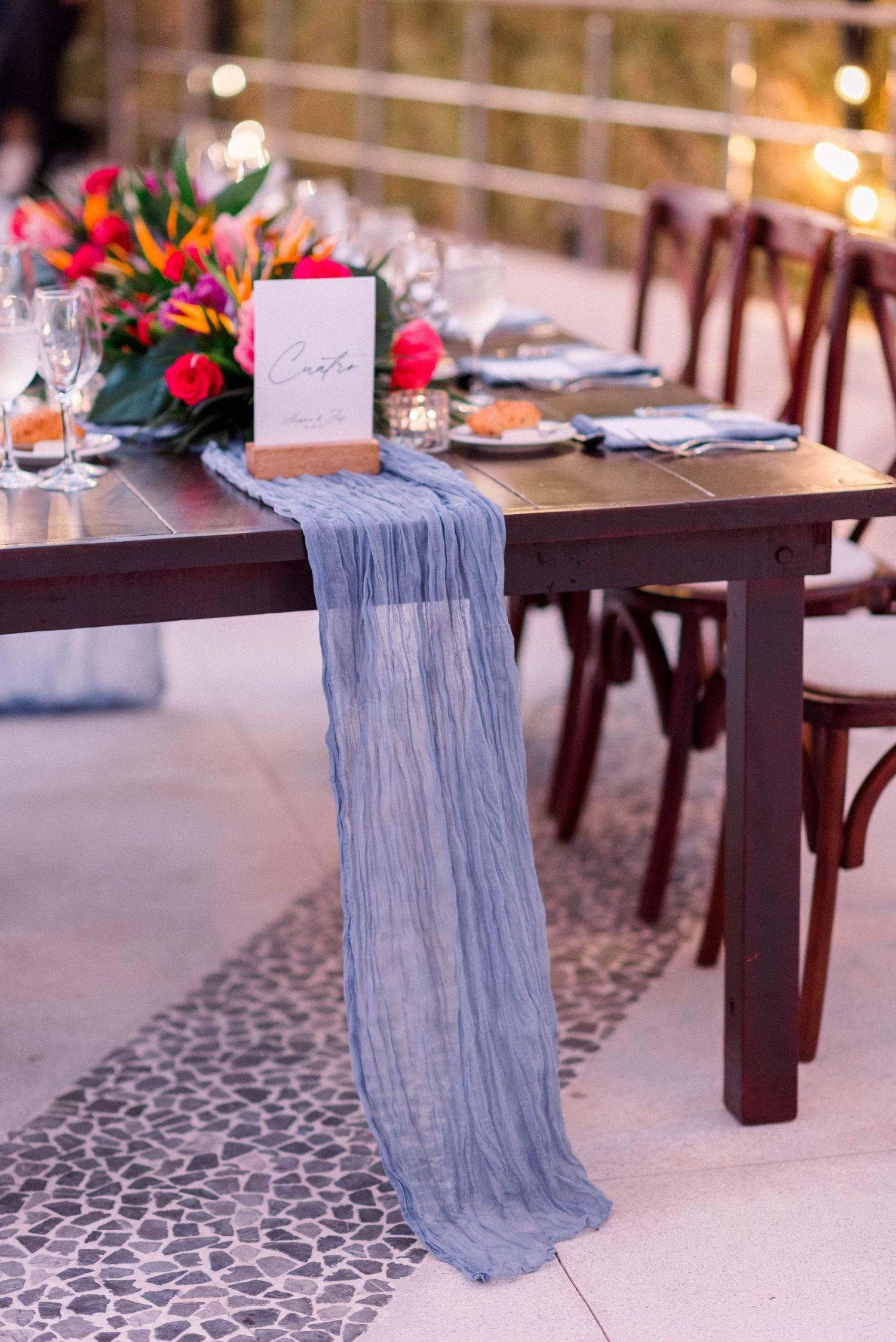 Wedding table decor featuring blue flowing runner and tropical floral arrangement.