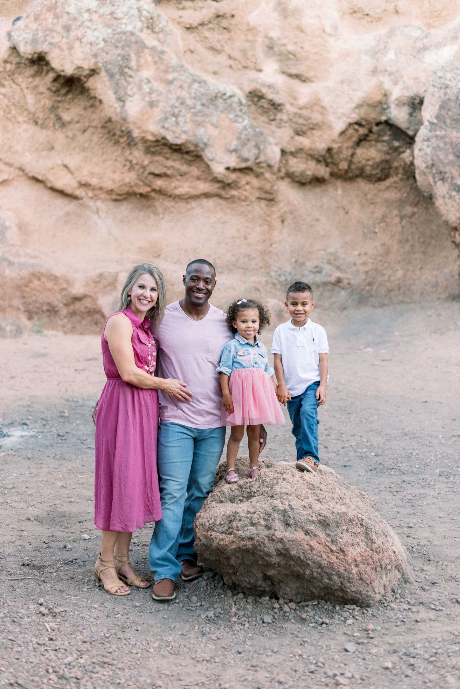 A family of four poses together against a rocky desert backdrop near a large boulder.