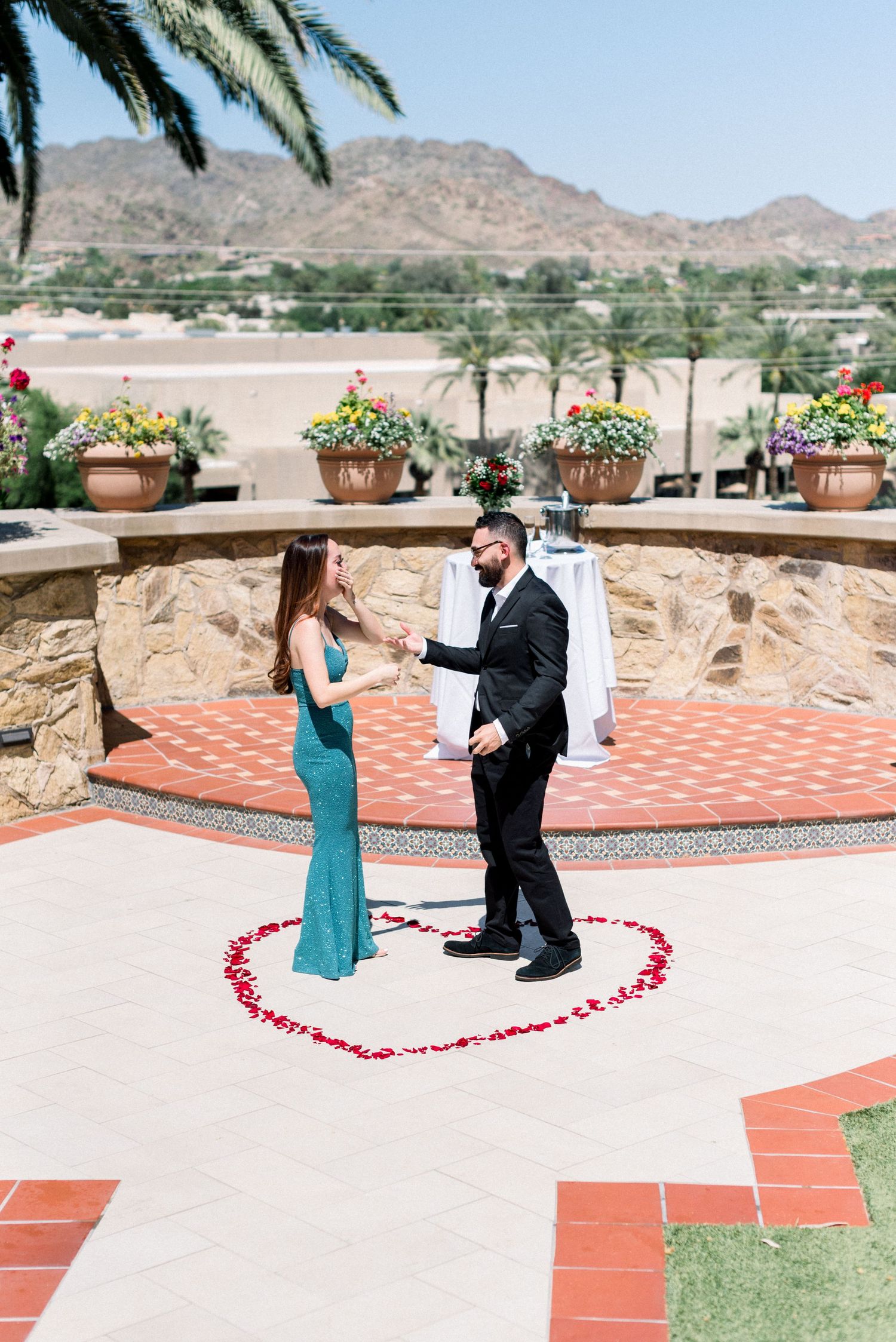 Couple stands inside heart made of rose petals during desert mountain proposal.