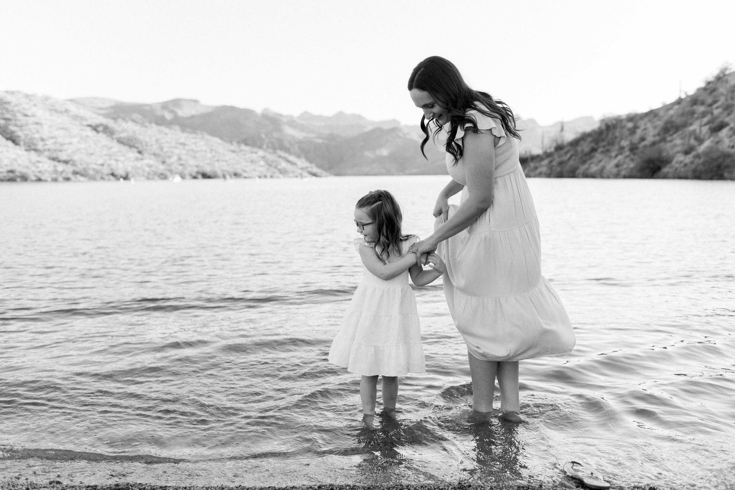 Mother and daughter holding hands while standing in calm lake waters.