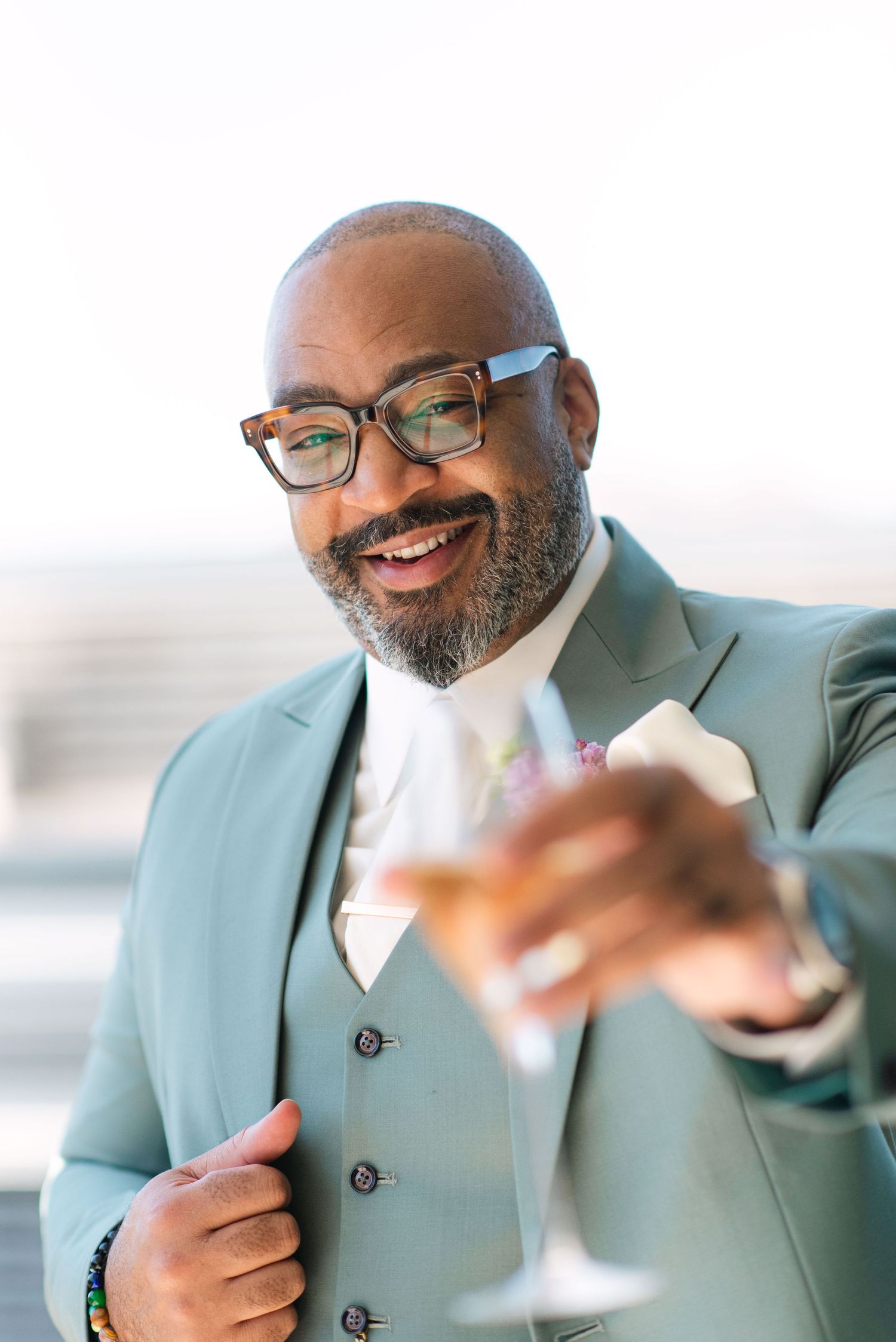 Professional wearing a mint green suit and glasses smiles while looking at something off camera.
