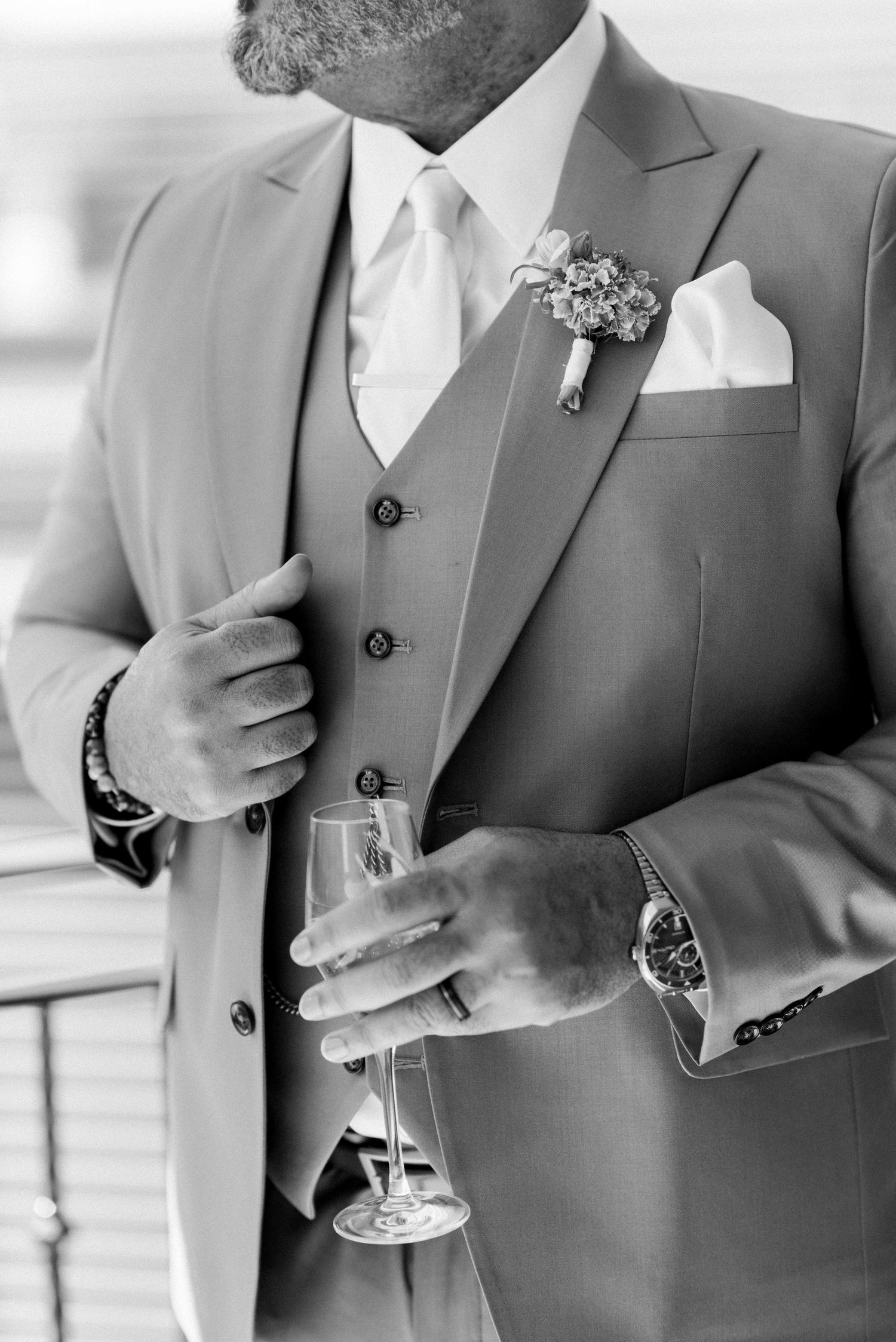 A close-up of a gray three-piece suit with boutonniere, pocket square, and champagne glass.