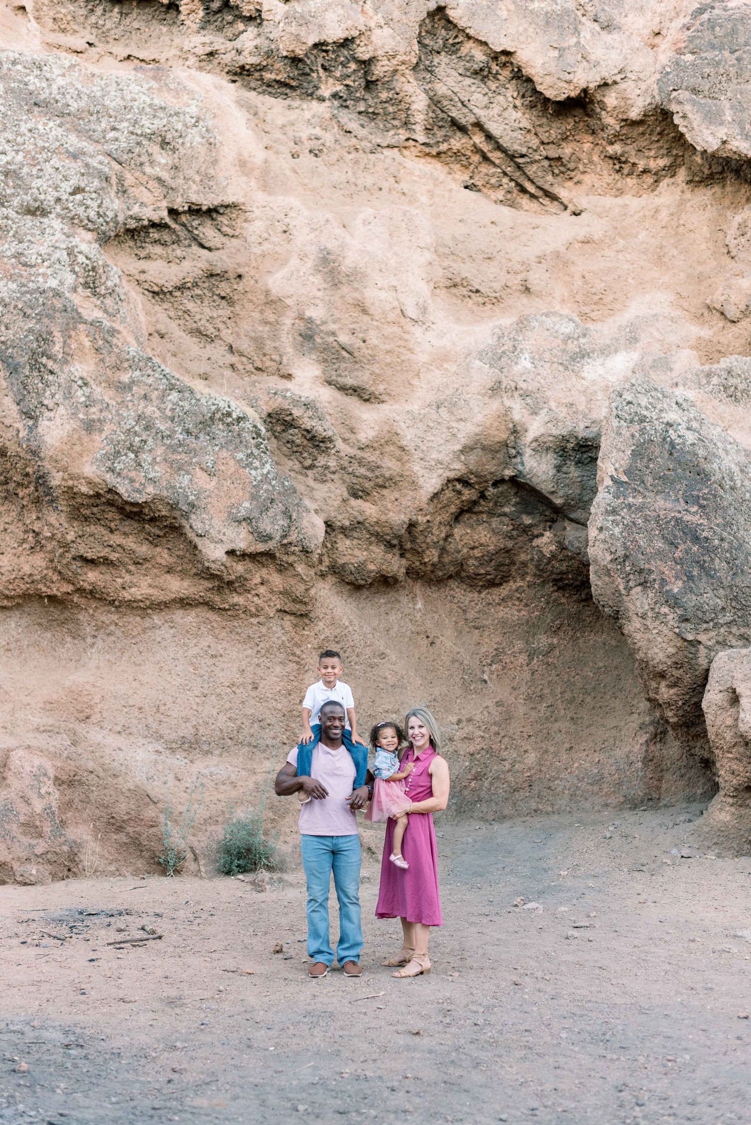 A group stands together against a rocky desert canyon wall in casual attire during a daytime outing.