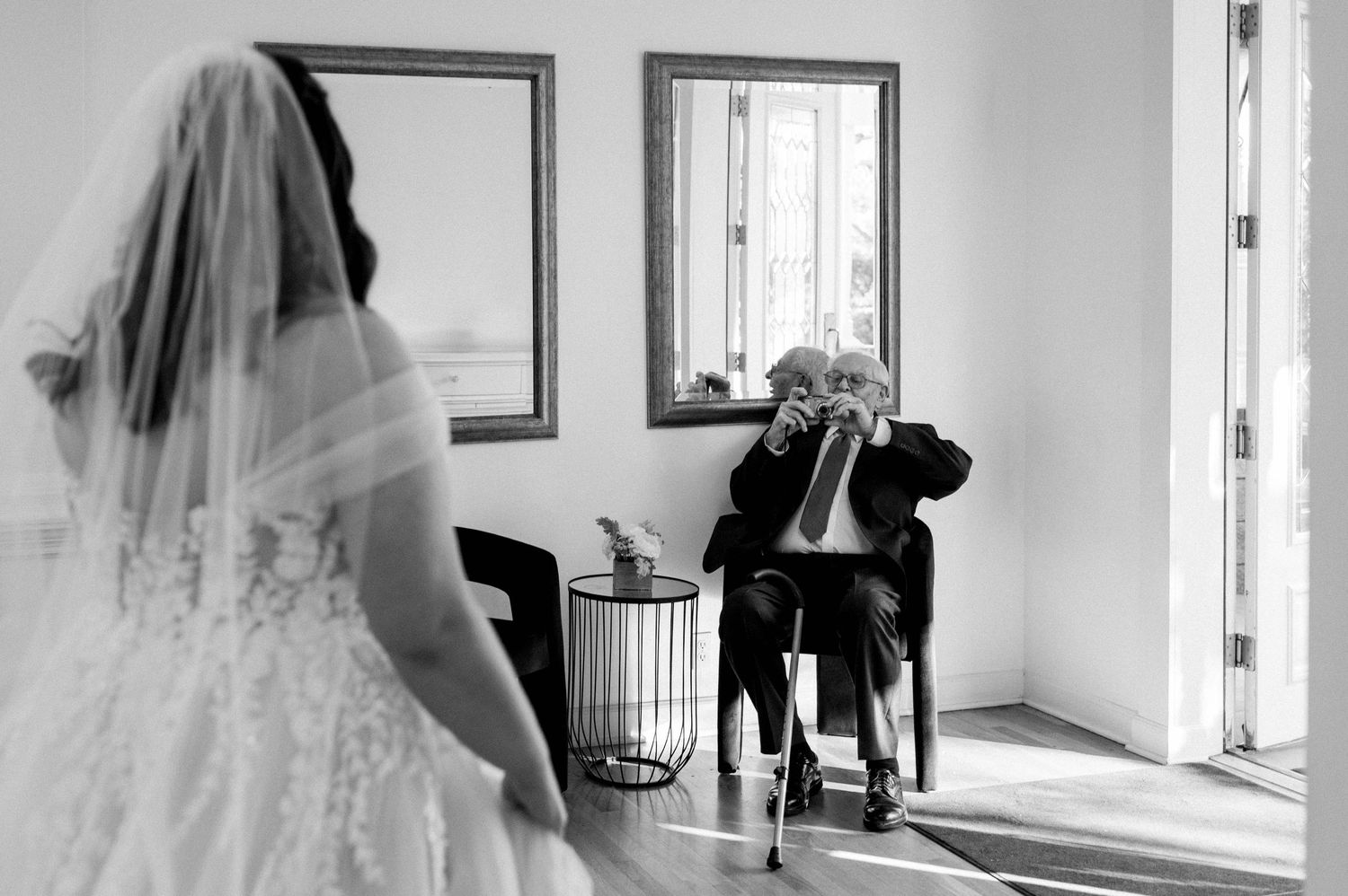 Black and white wedding photo showing emotional first look moment in sunlit room.