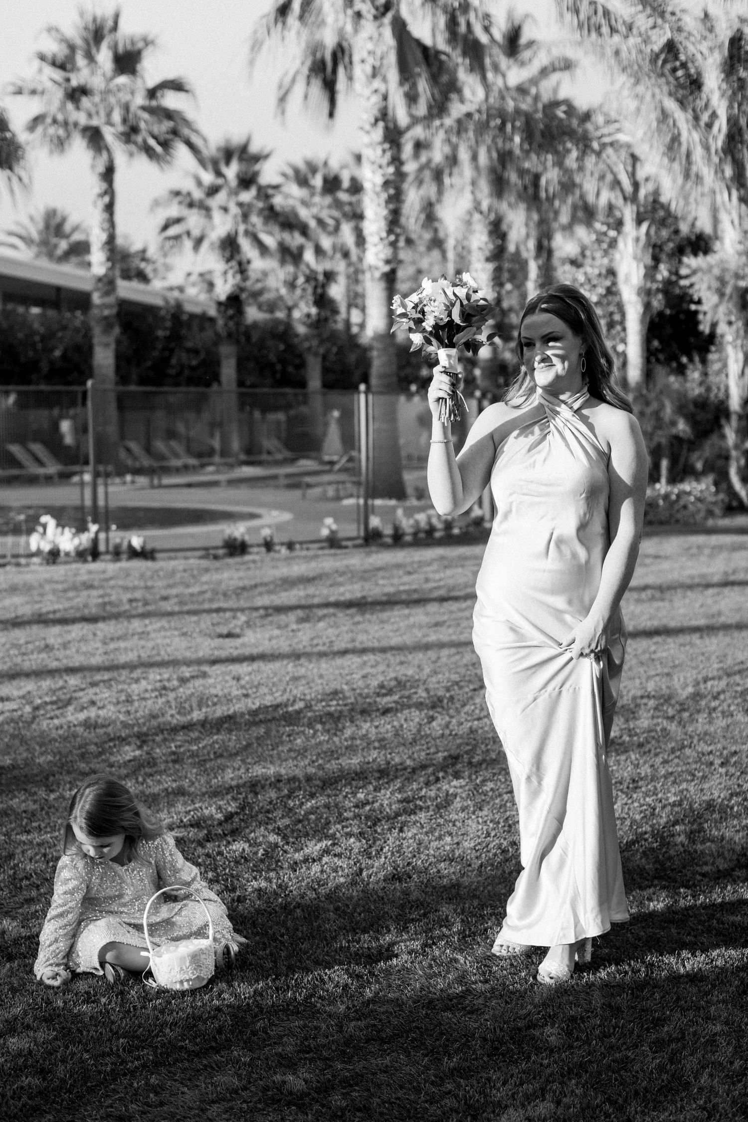 Black and white photo of bride holding bouquet on lawn with palm trees.