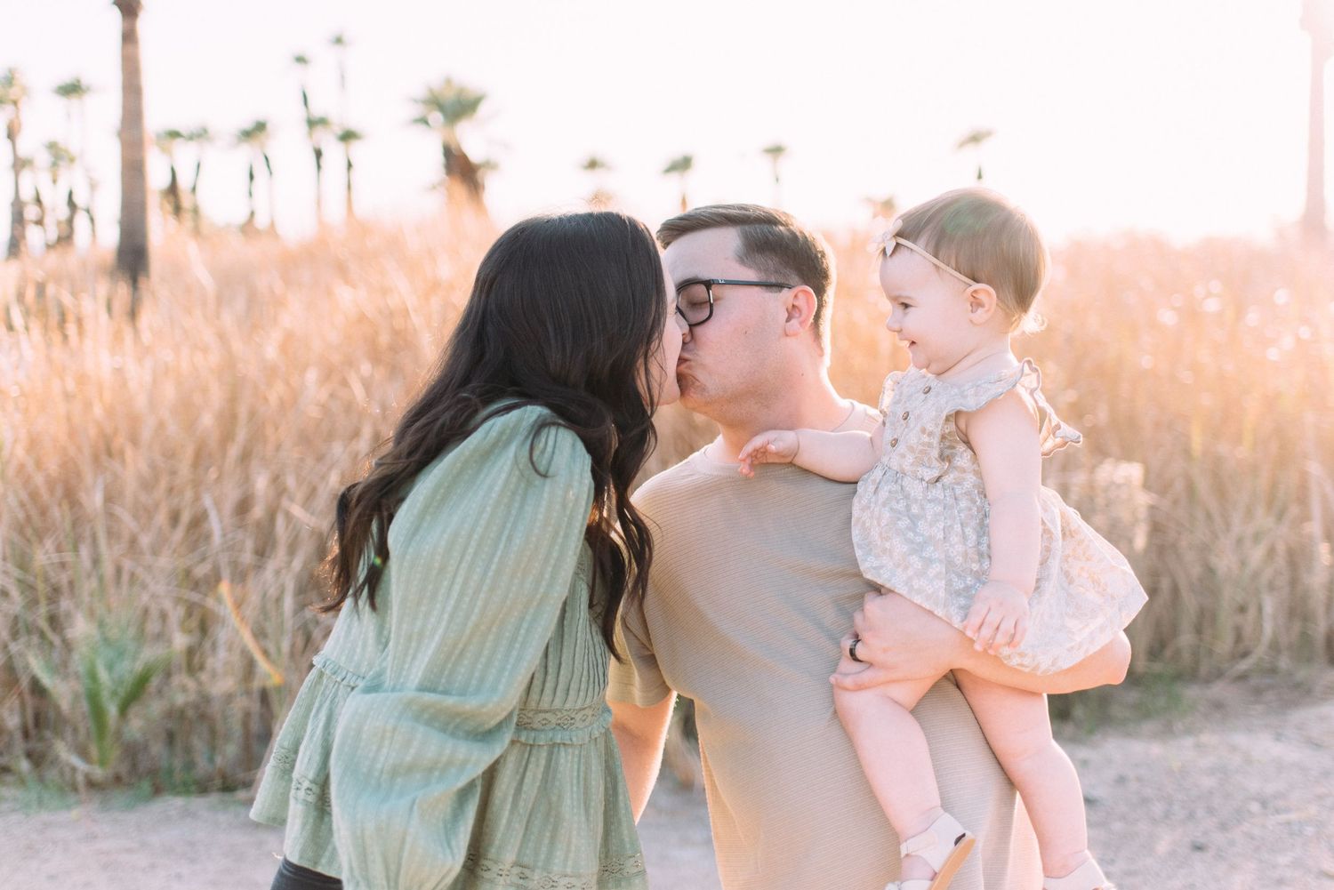 A family shares a tender moment together on a path with palm trees at sunset.