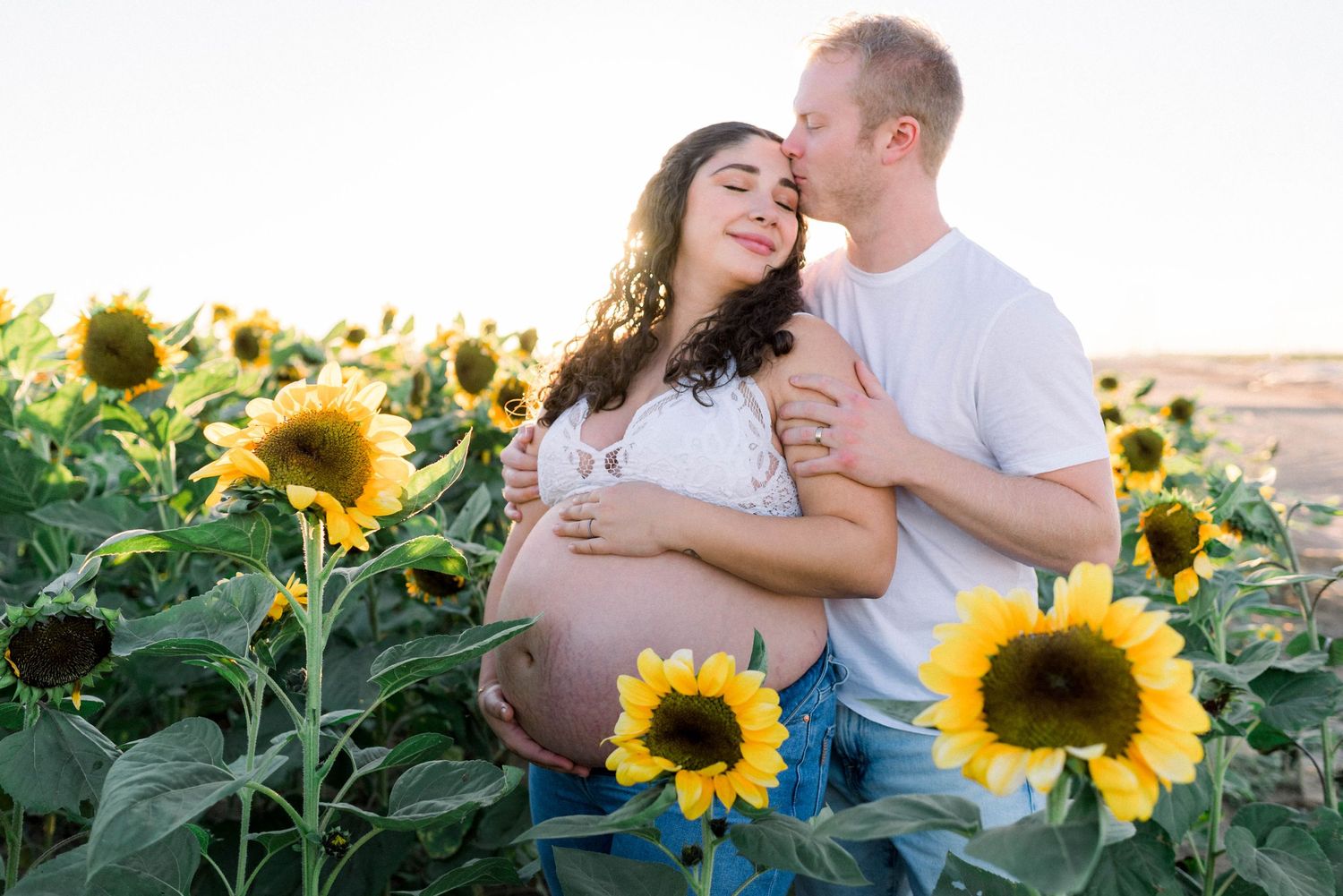 Maternity photo of couple kissing in sunflower field