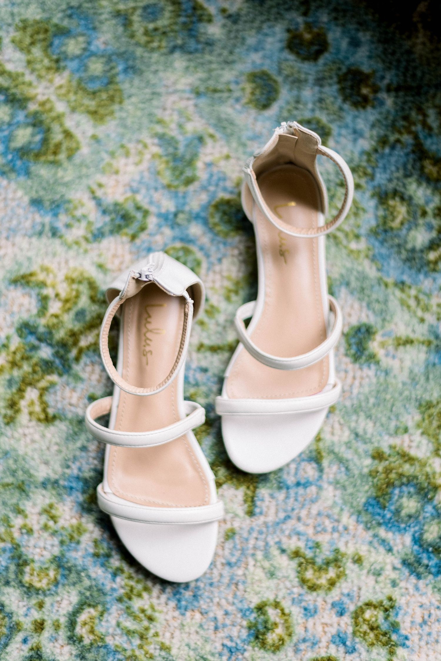 Elegant white strappy sandals on floral patterned carpet.