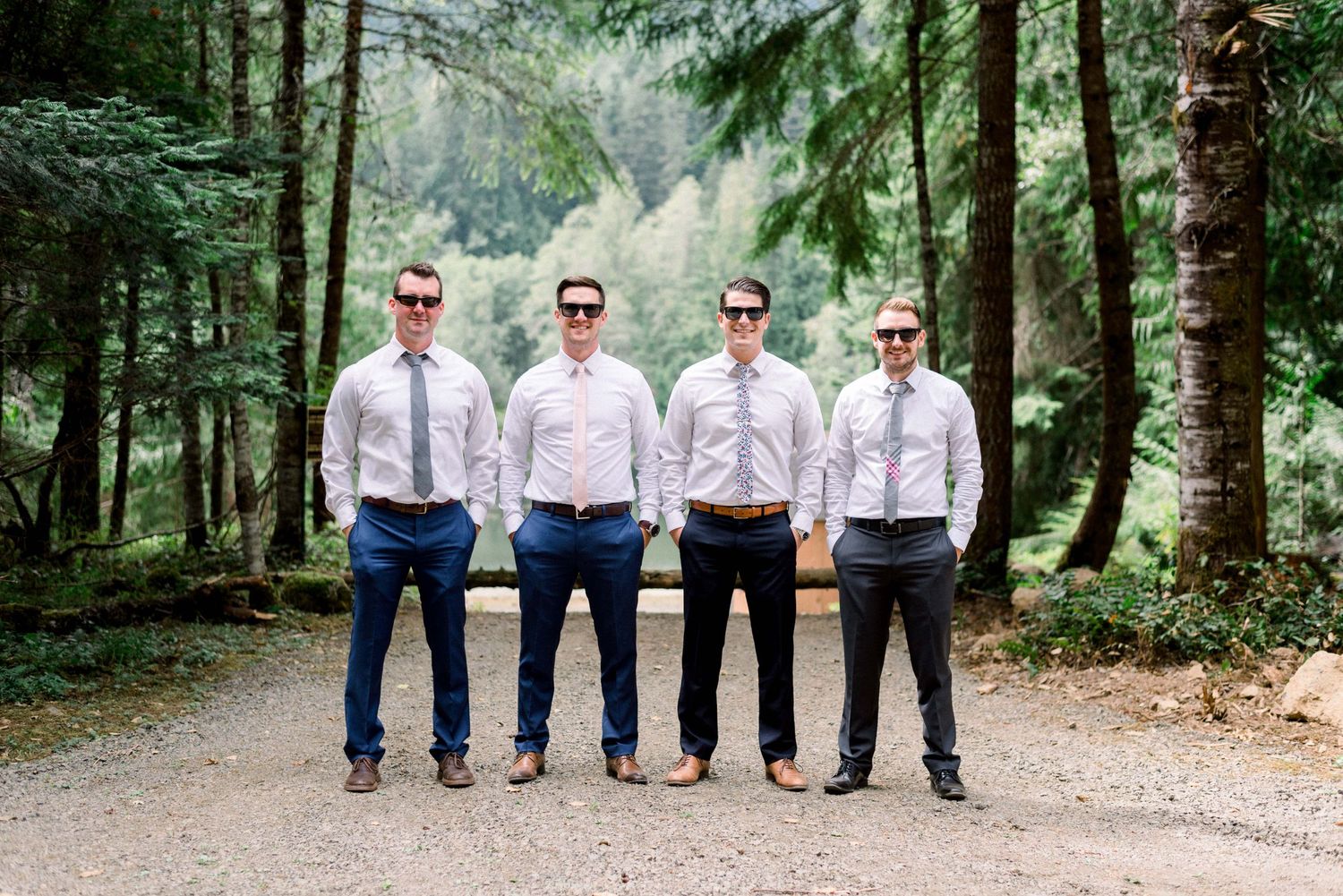 Groomsmen in matching attire pose together on a forest path.