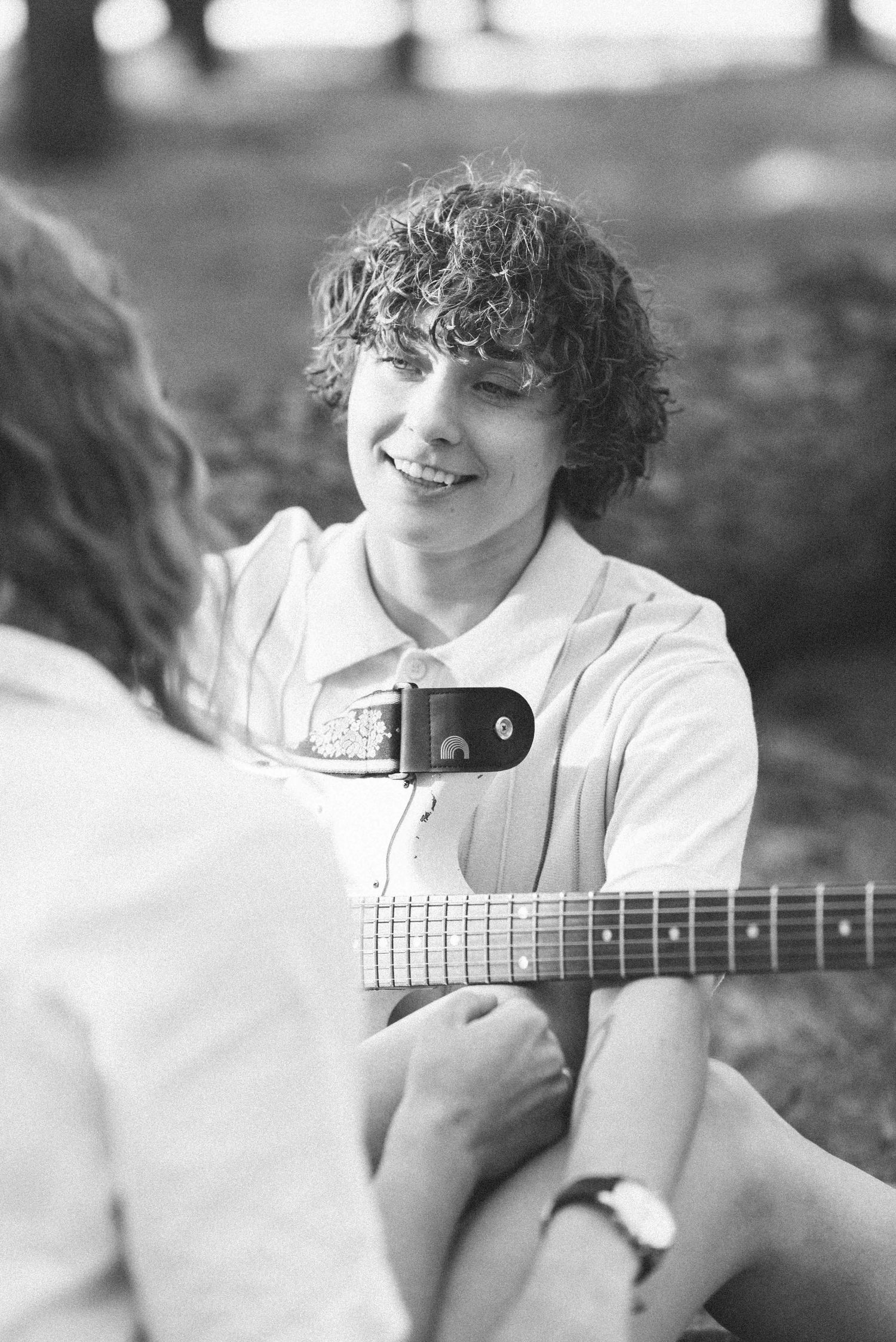 Black and white candid shot of couple with electric guitar in natural setting.