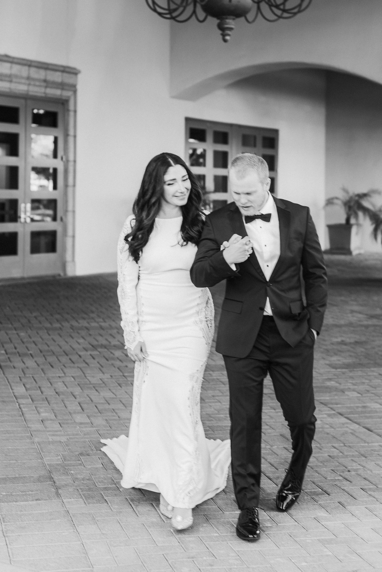 Couple walking and laughing together at wedding, bride in white gown and groom in black tuxedo.
