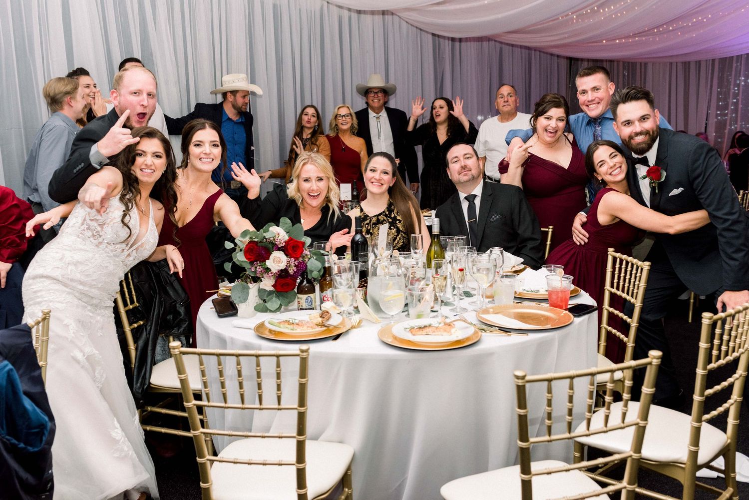 Wedding guests pose playfully around dining table at reception.