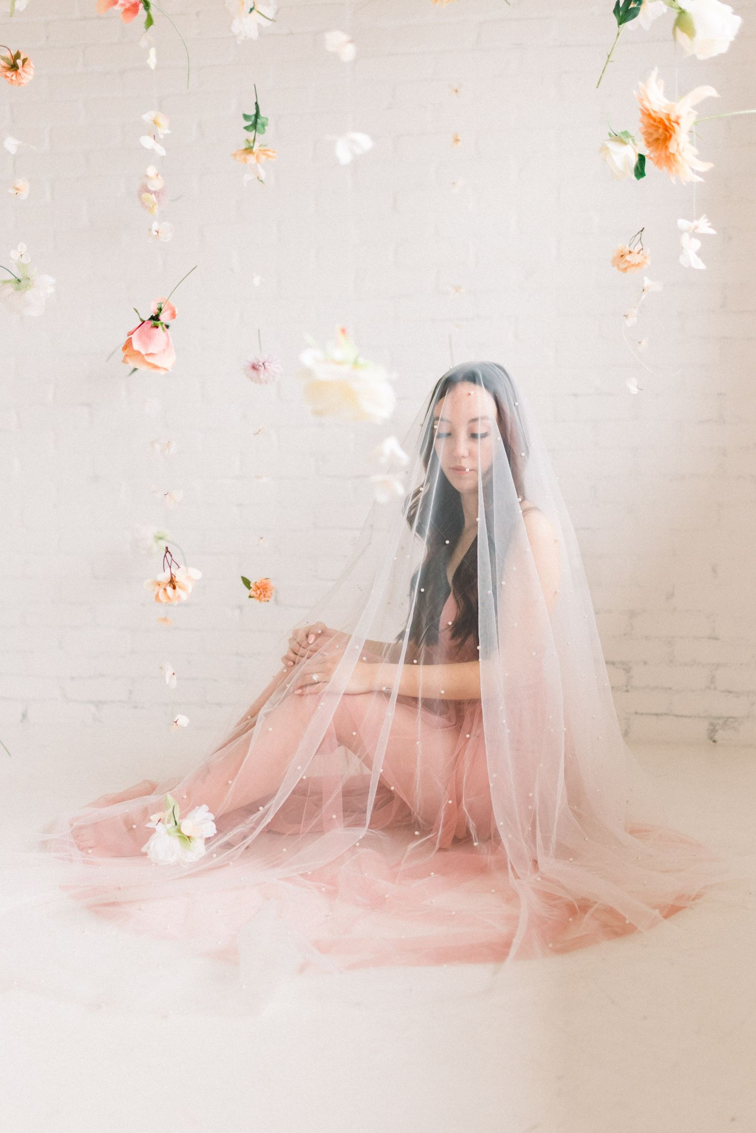 Dreamy bridal portrait with floating flowers and sheer veil in pink tulle dress.