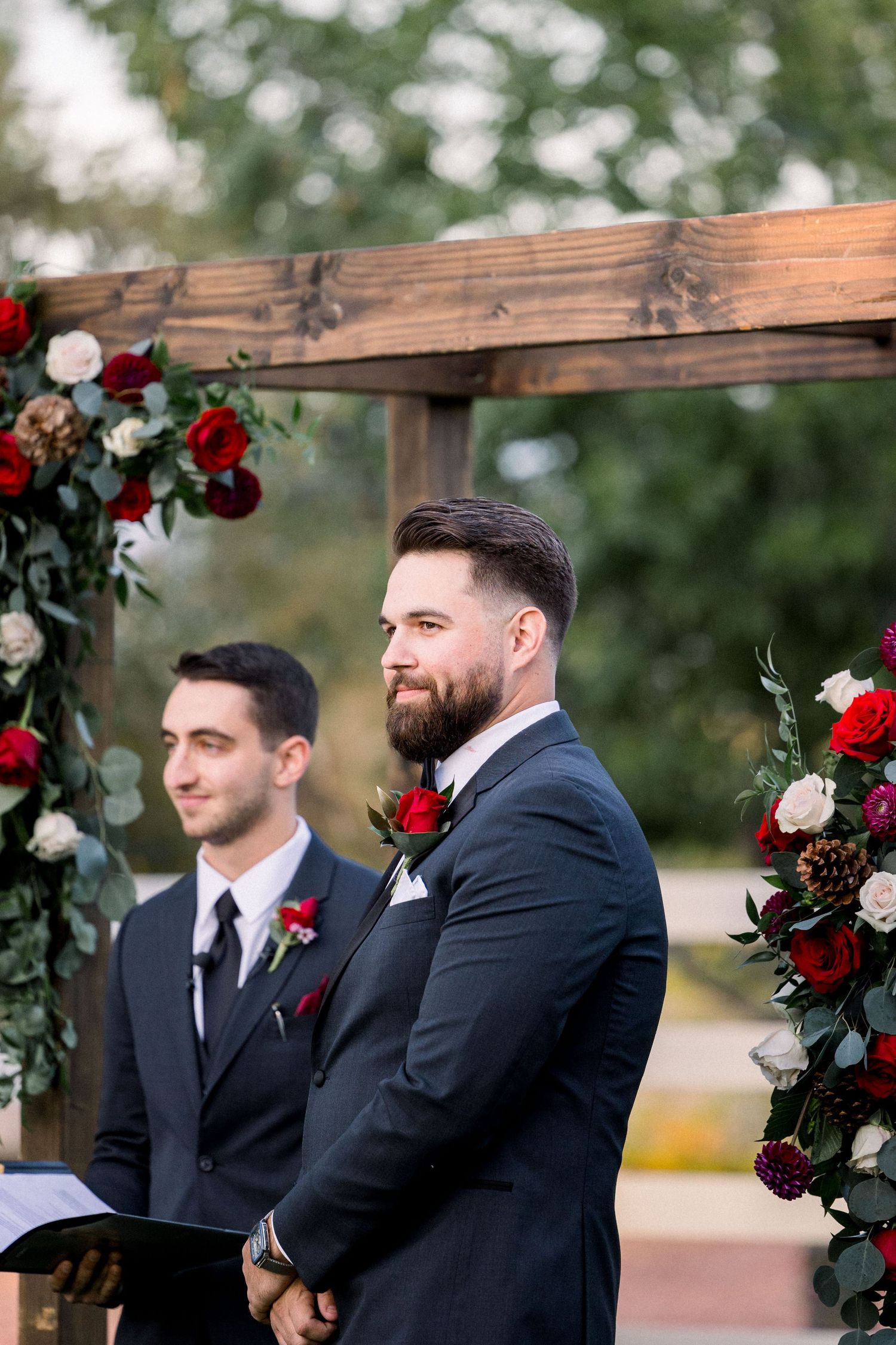 A wooden wedding arch adorned with red and white flowers frames the ceremony space.