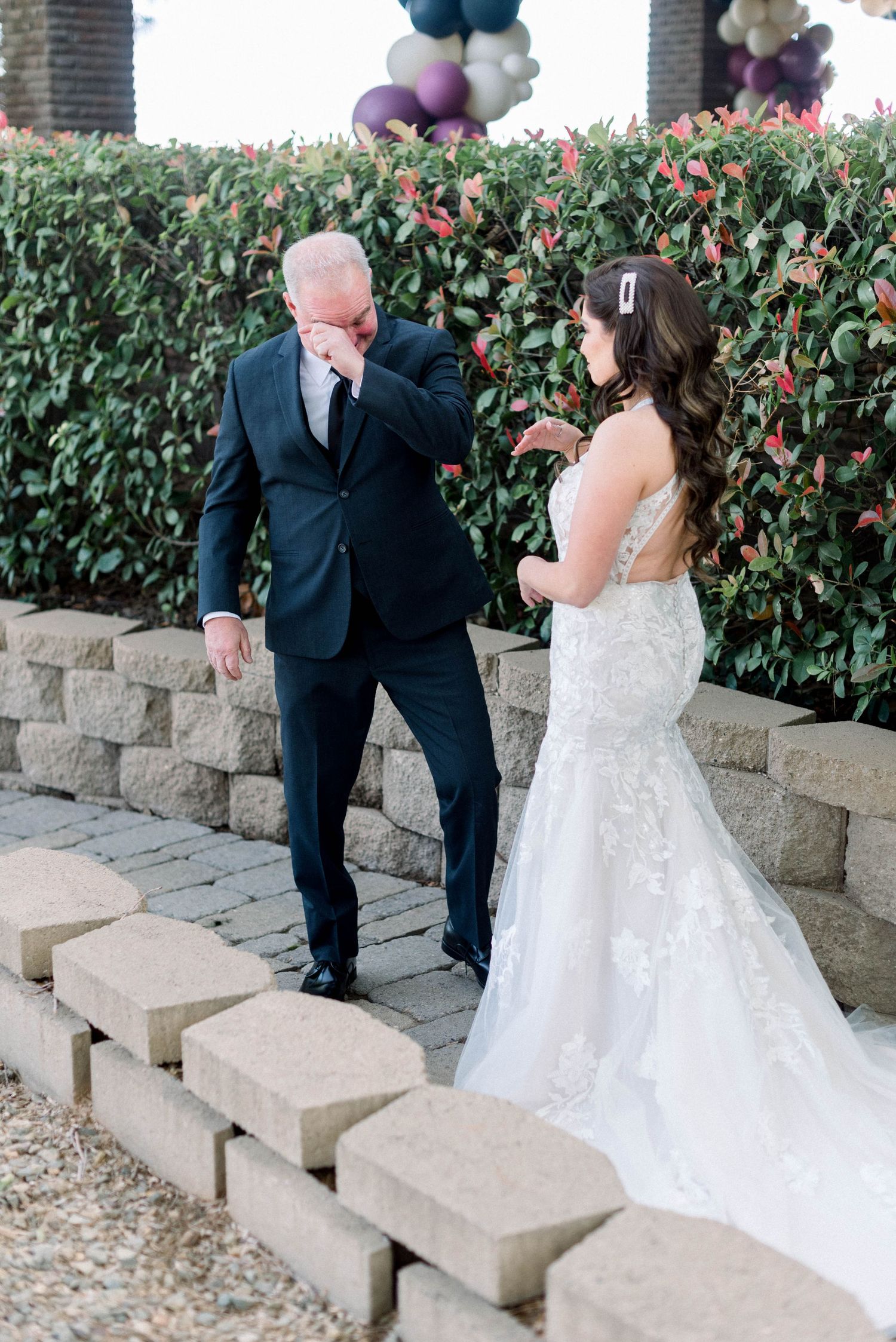 An emotional first look reaction between a couple on stone steps with a decorative hedge backdrop.