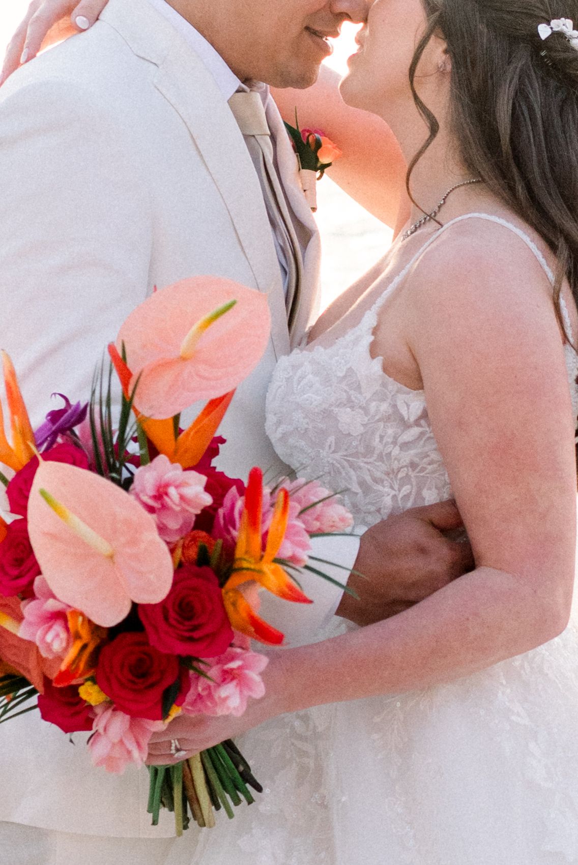 Close-up of wedding couple with tropical coral and pink flower bouquet.