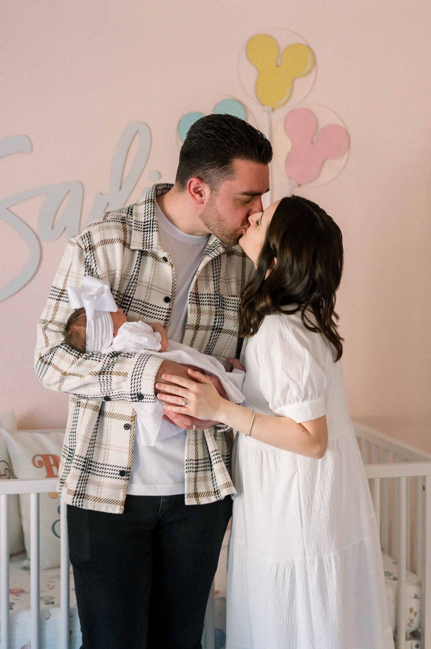 Couple shares tender moment in nursery with pastel decor while holding their newborn.