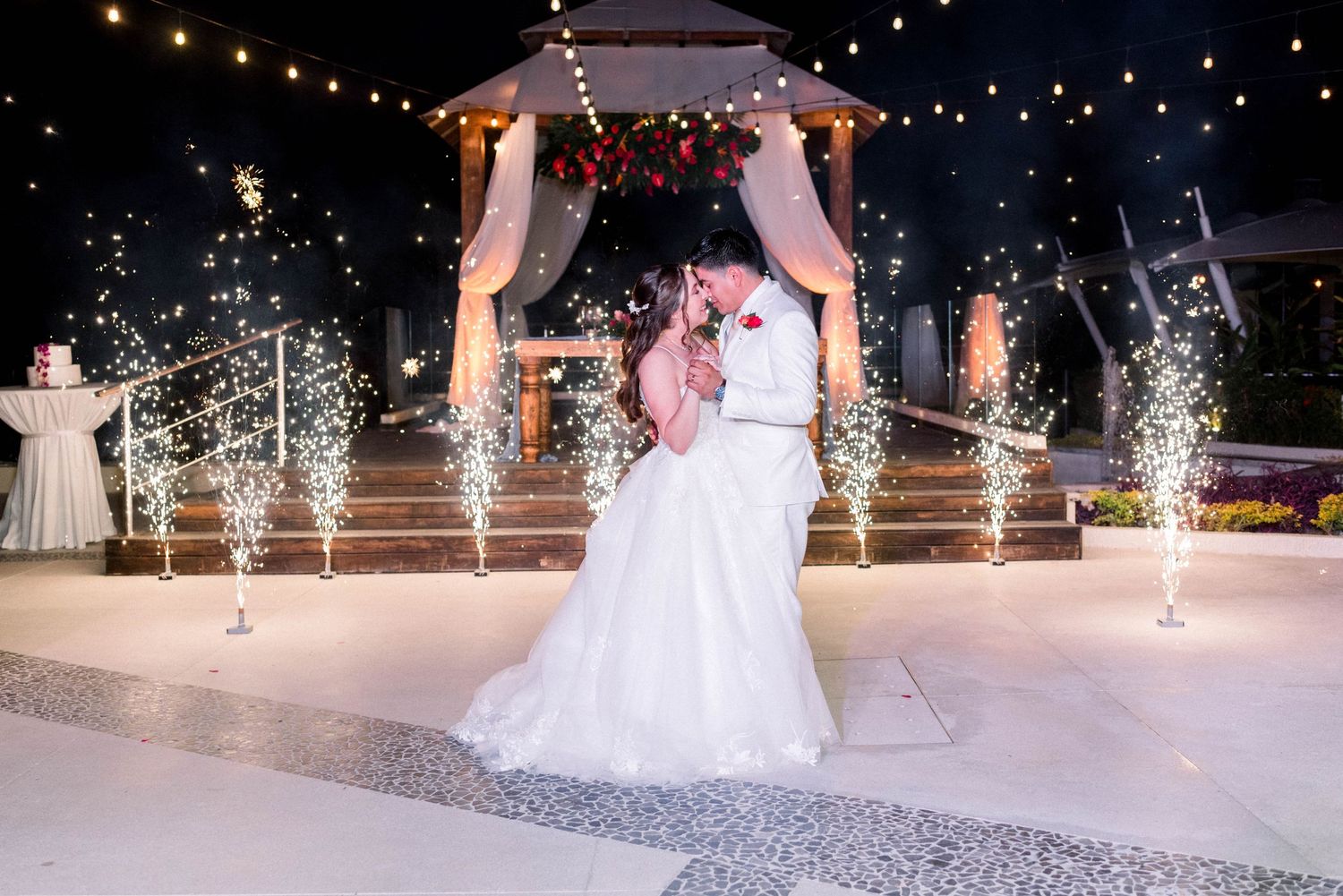 A couple shares their first dance under a gazebo with sparklers and string lights creating a magical atmosphere.