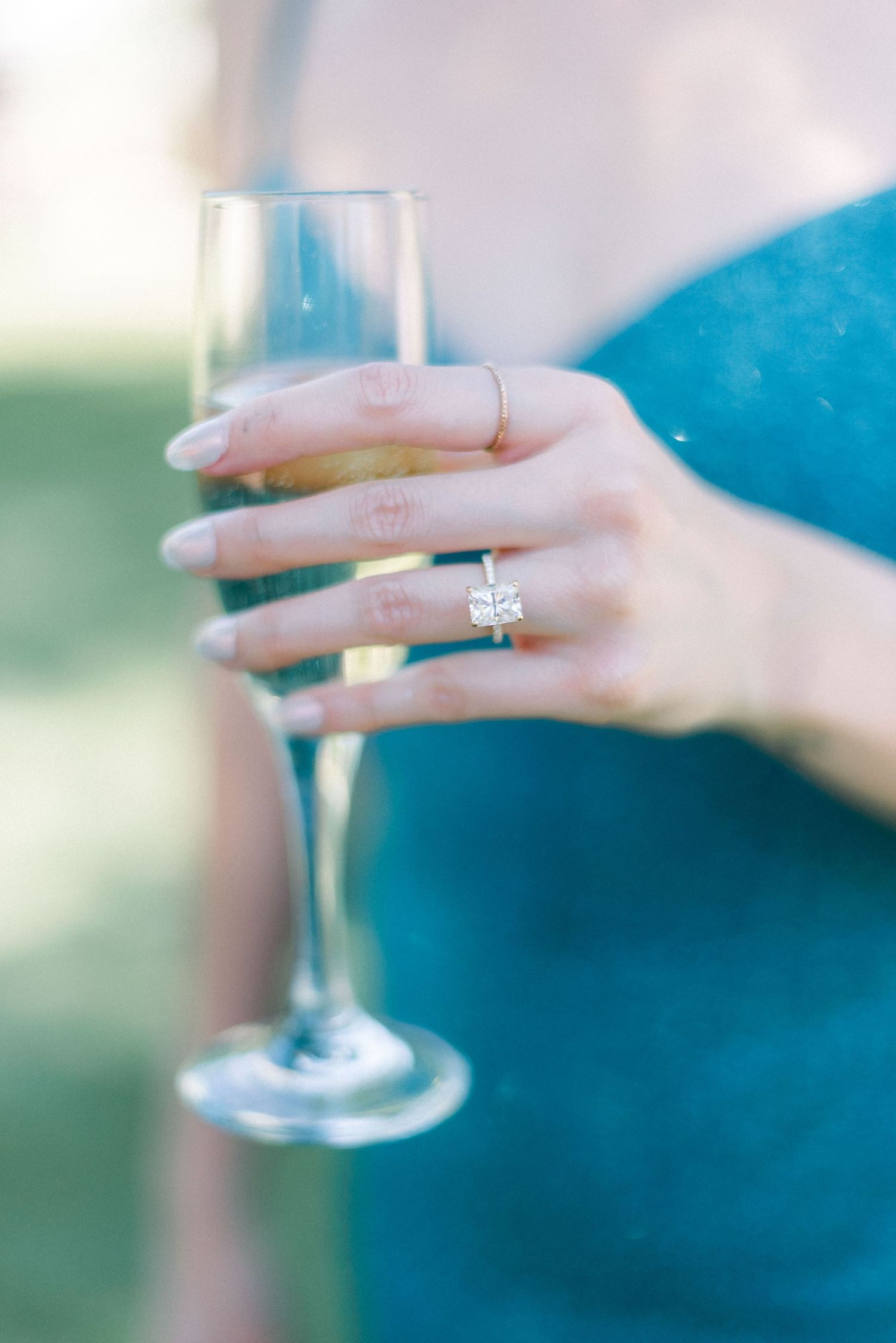 An elegant champagne glass held by a hand wearing a sparkling engagement ring.