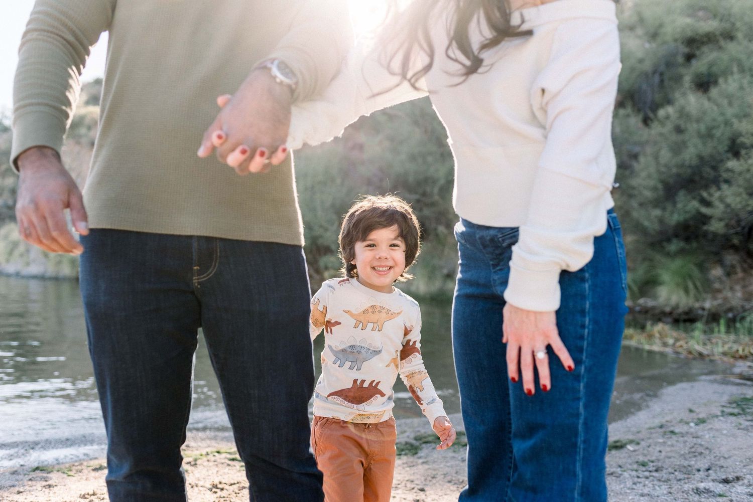A family walks together holding hands on a nature path during a sunny afternoon photo session.