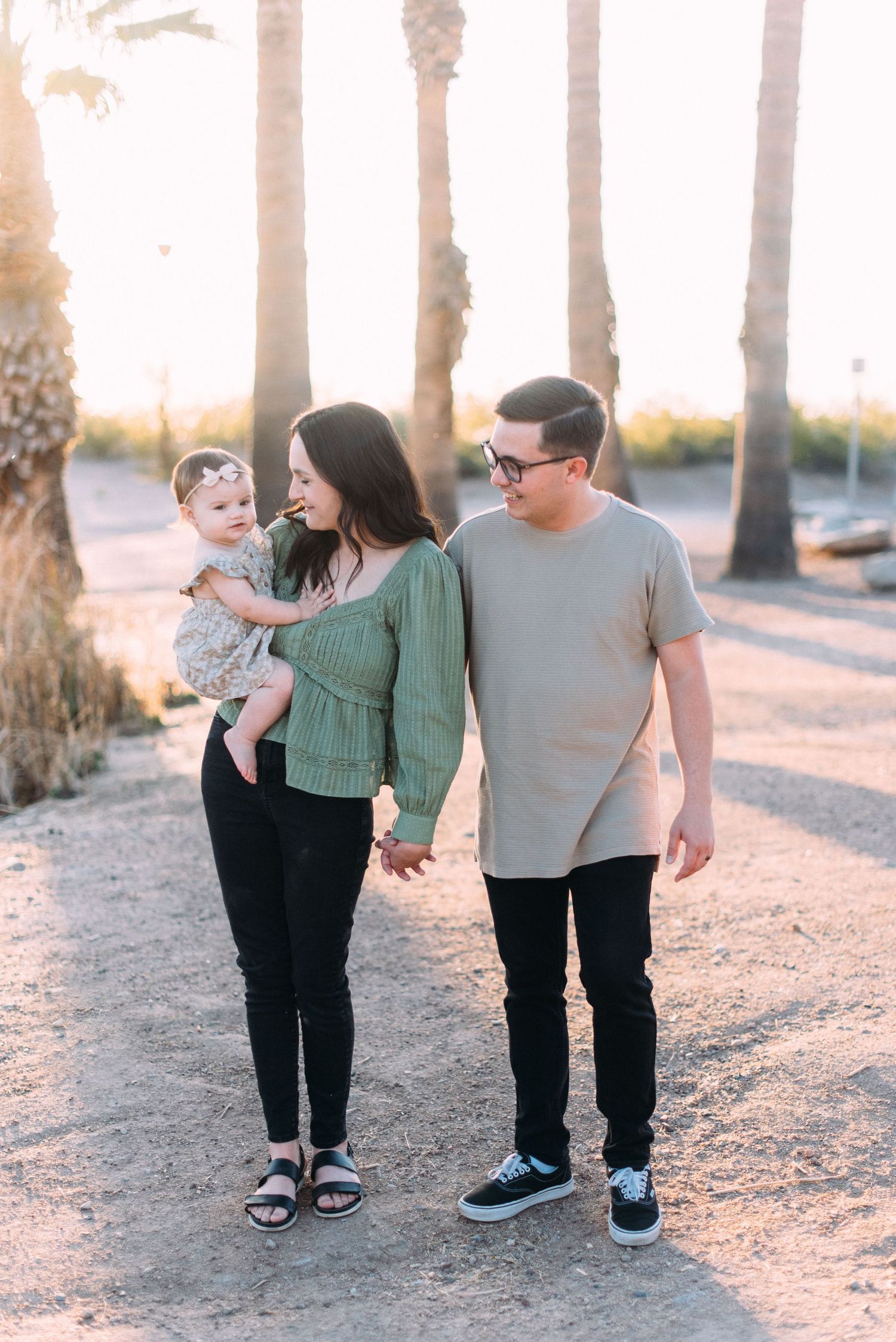 Family strolling together on sandy path with palm trees in golden evening light.
